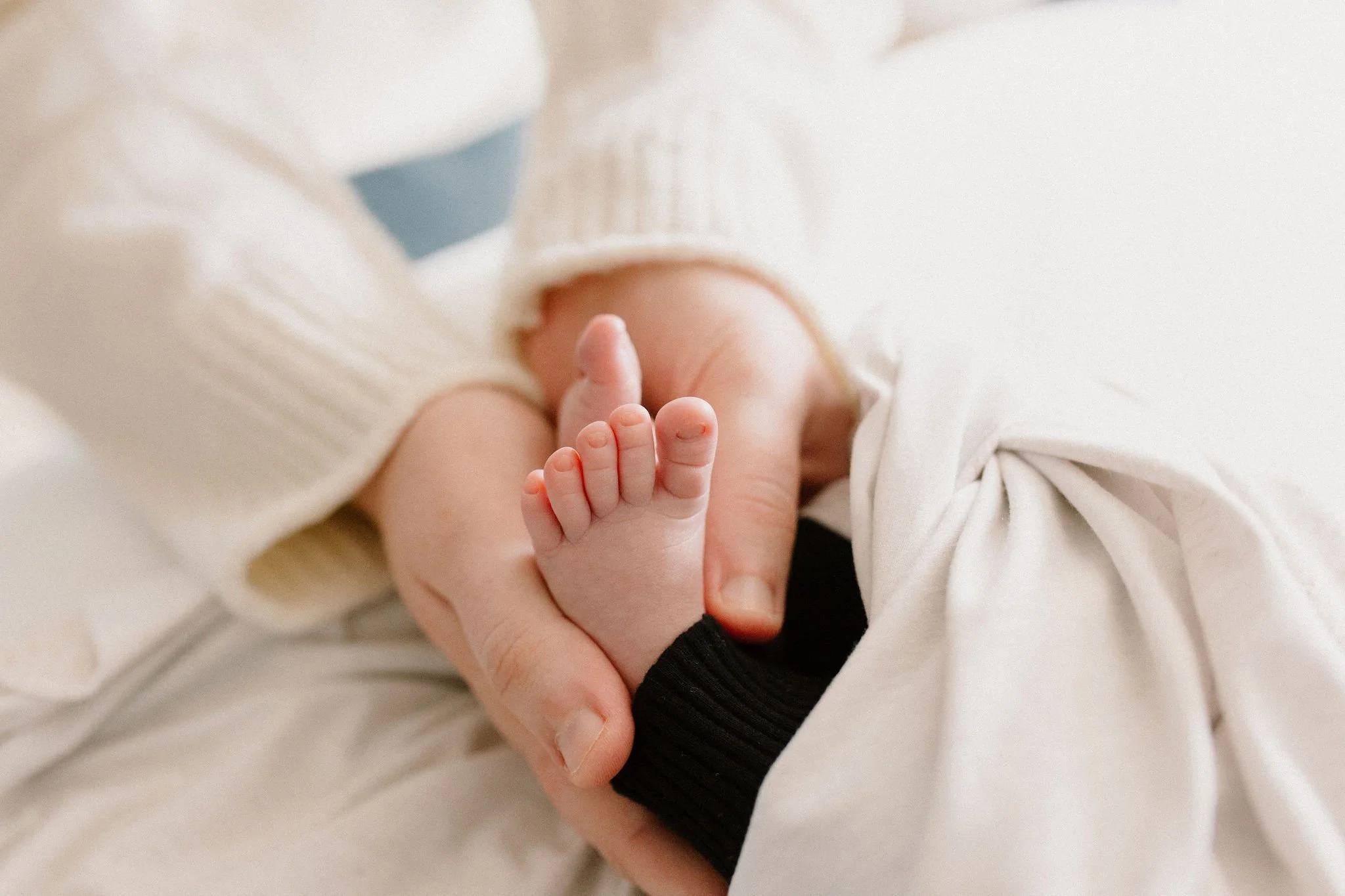 close up photo of newborn feet and toes being held by mom in neutral nursery