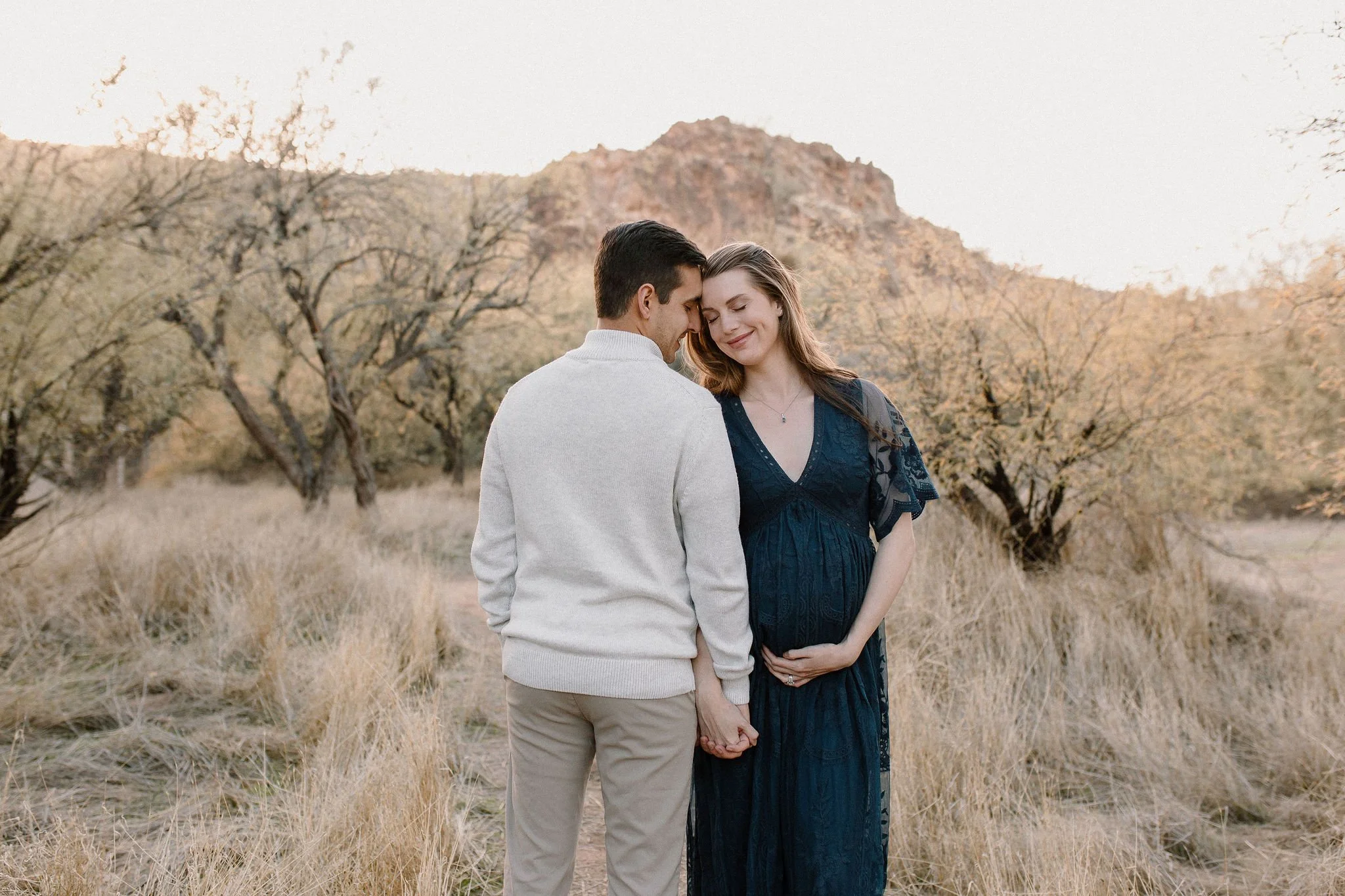 pregnant mom holding belly cuddling with dad in desert maternity photoshoot in Gilbert, Arizona