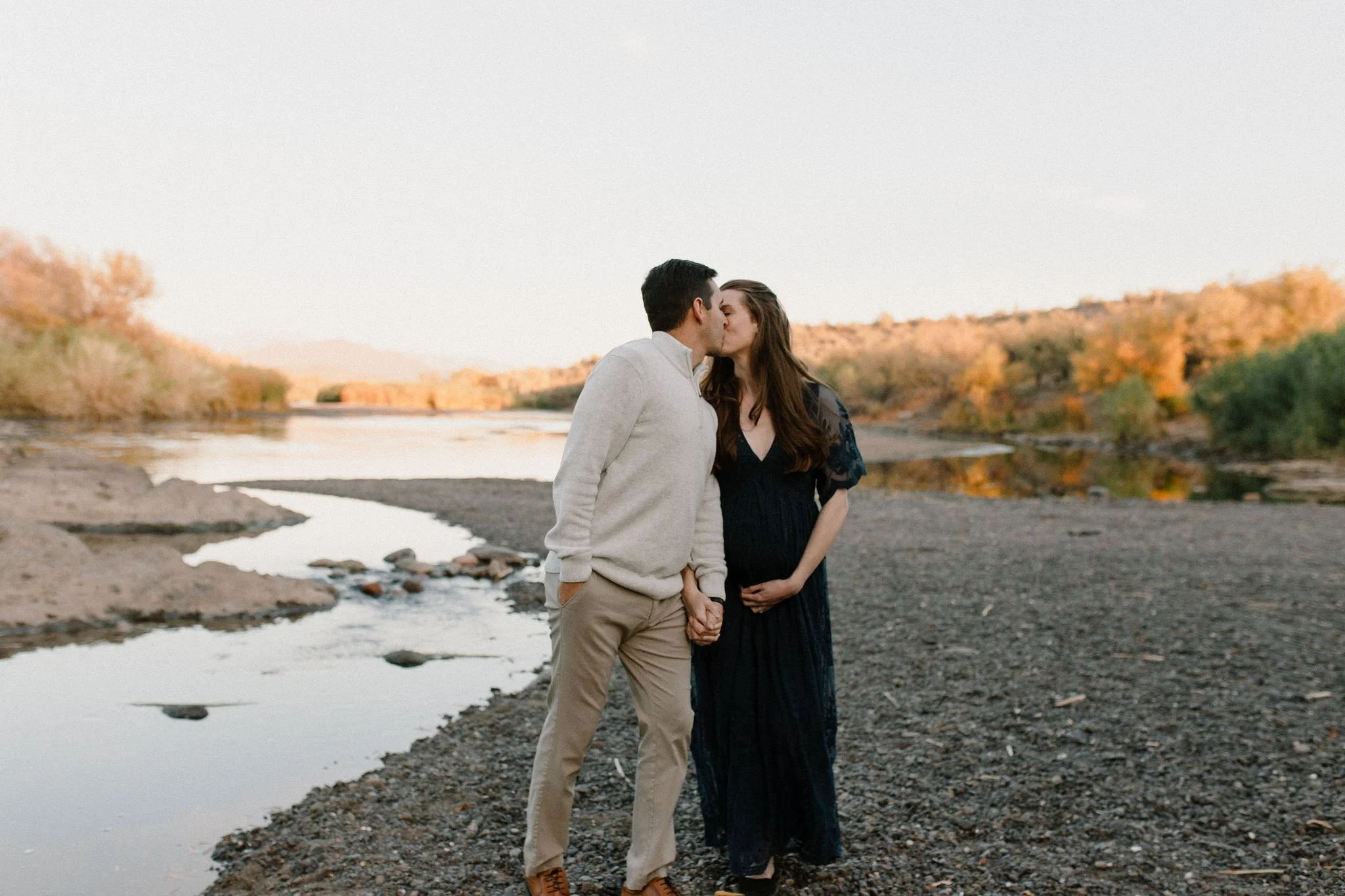 pregnant mom and dad walking and kissing by Salt River in Mesa maternity photography session
