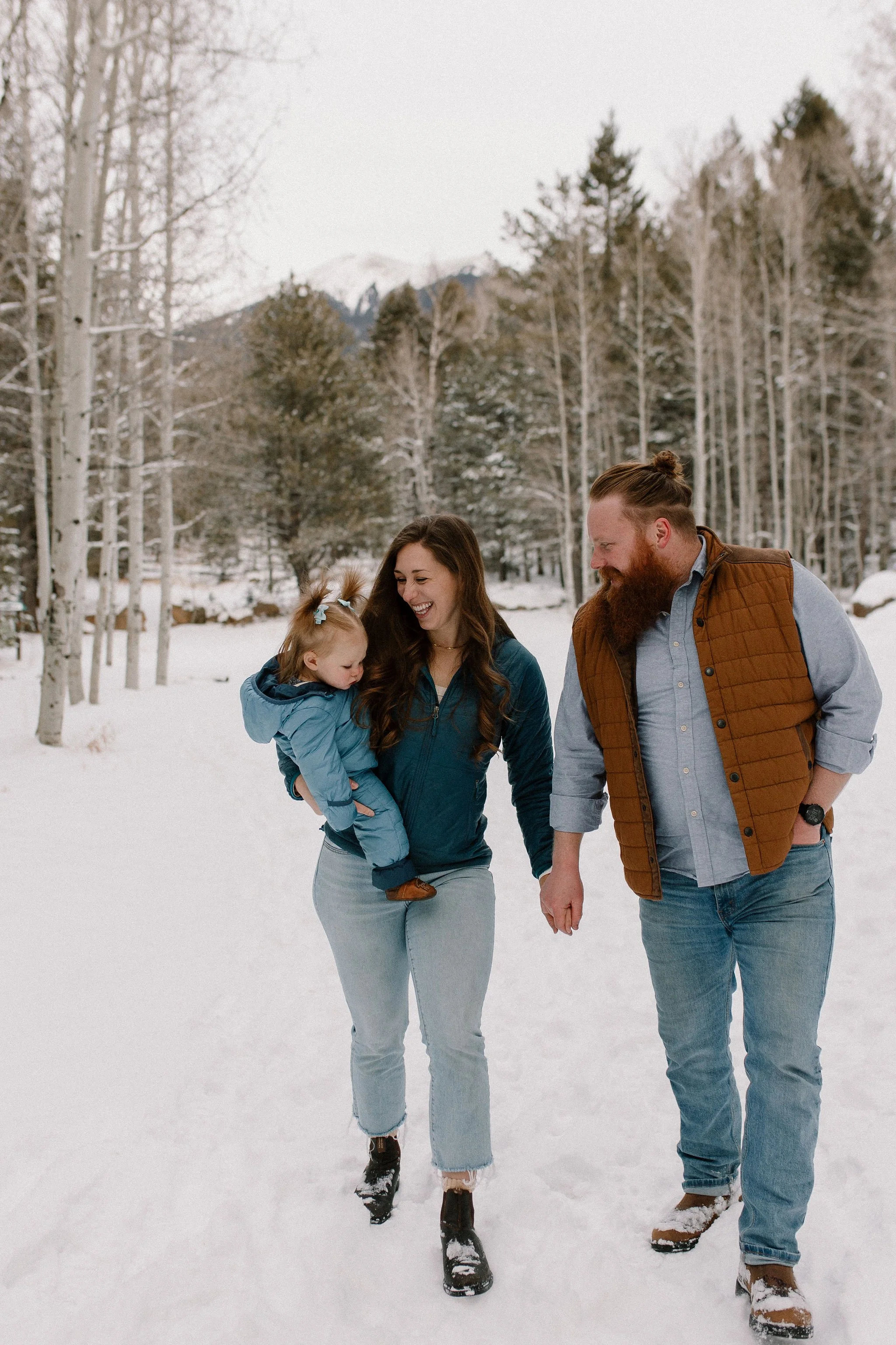 family of three walking together in the snow during winter family photo session in Flagstaff, Arizona