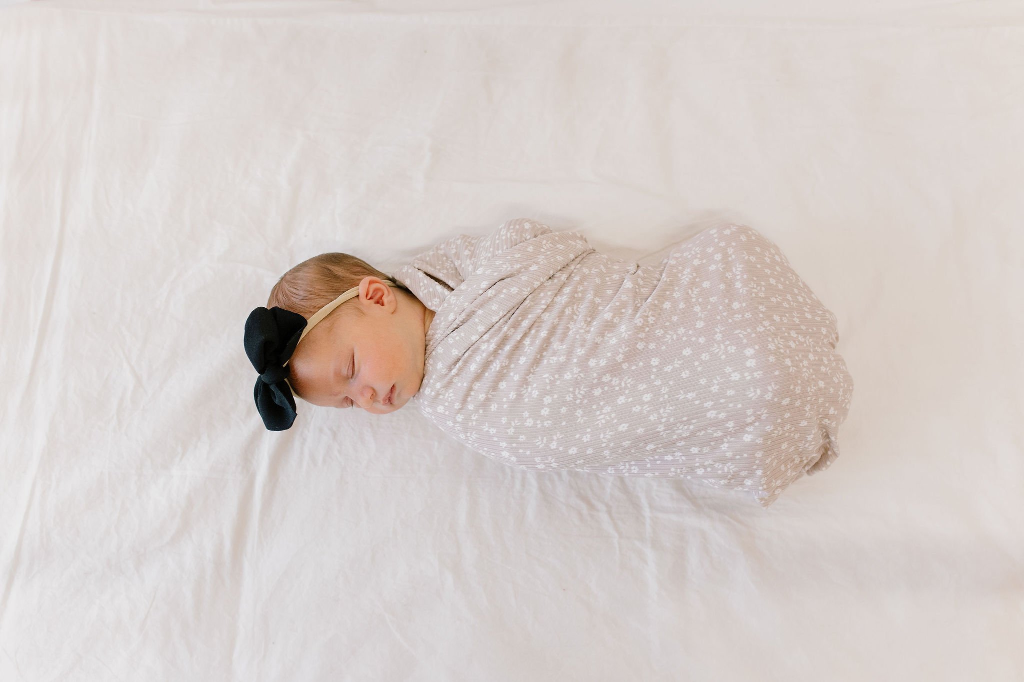 swaddled newborn baby girl sleeping in neutral crib