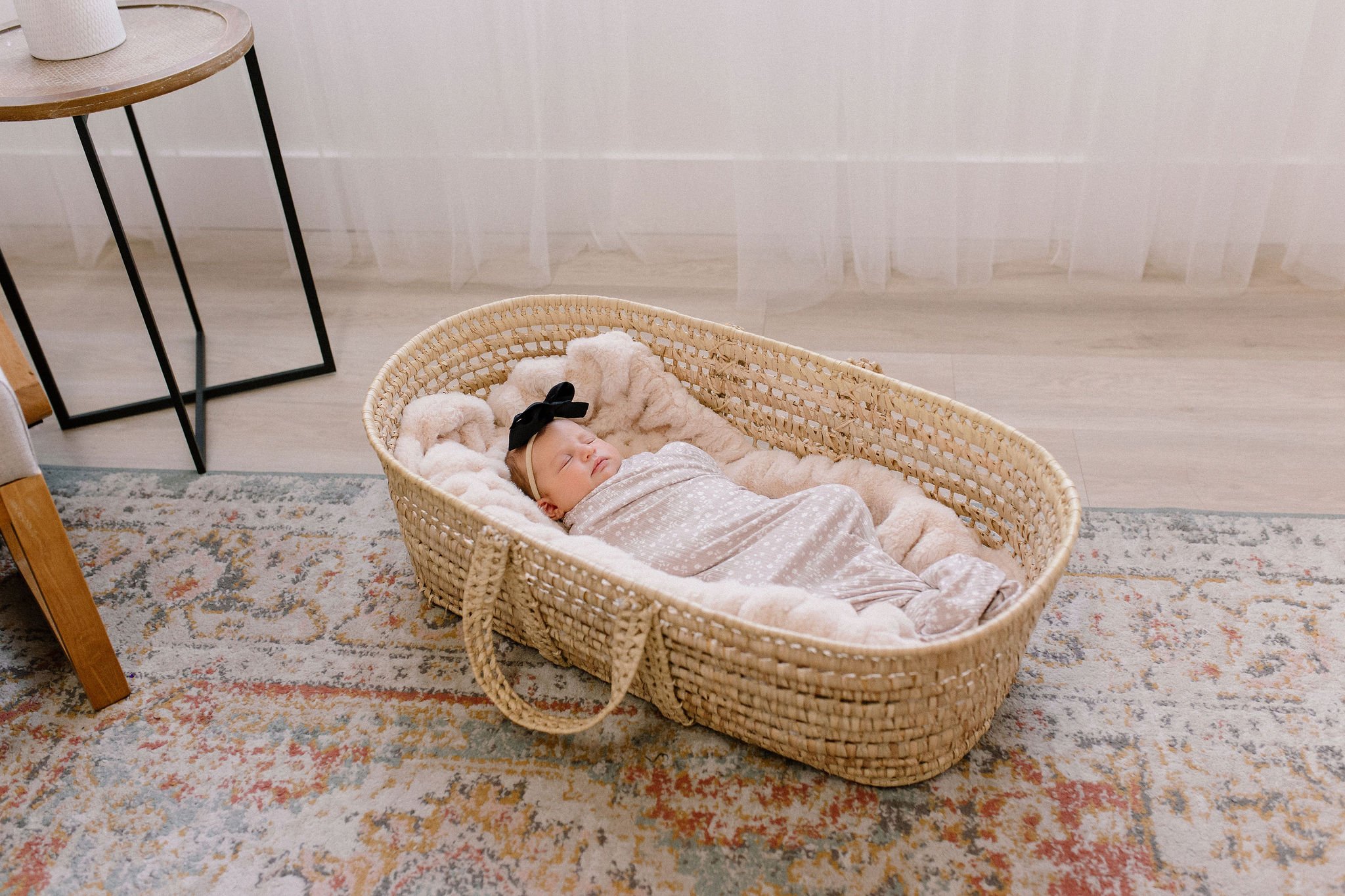 swaddled newborn baby girl sleeping in Moses basket in neutral nursery