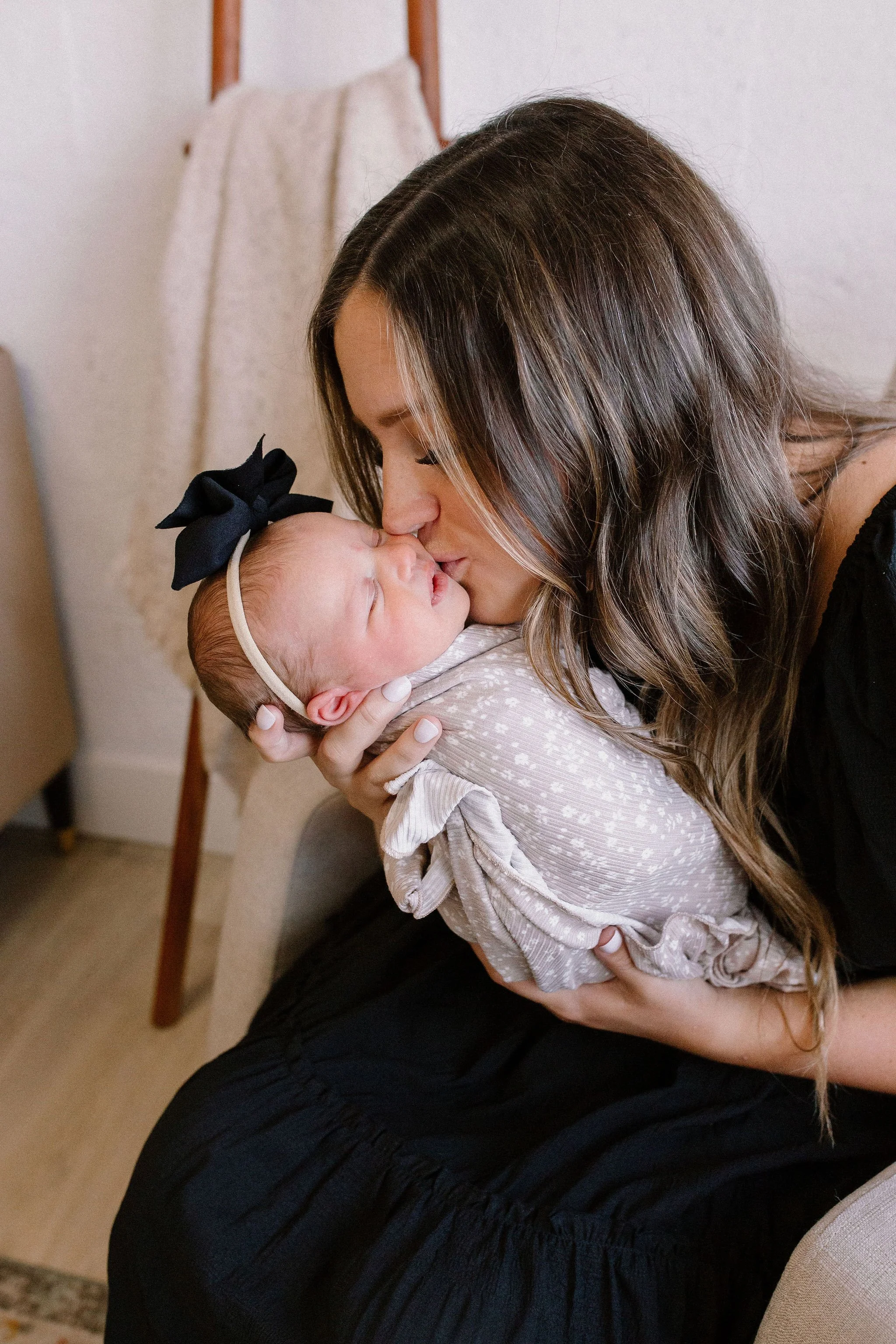 mom kissing newborn baby girl in neutral nursery