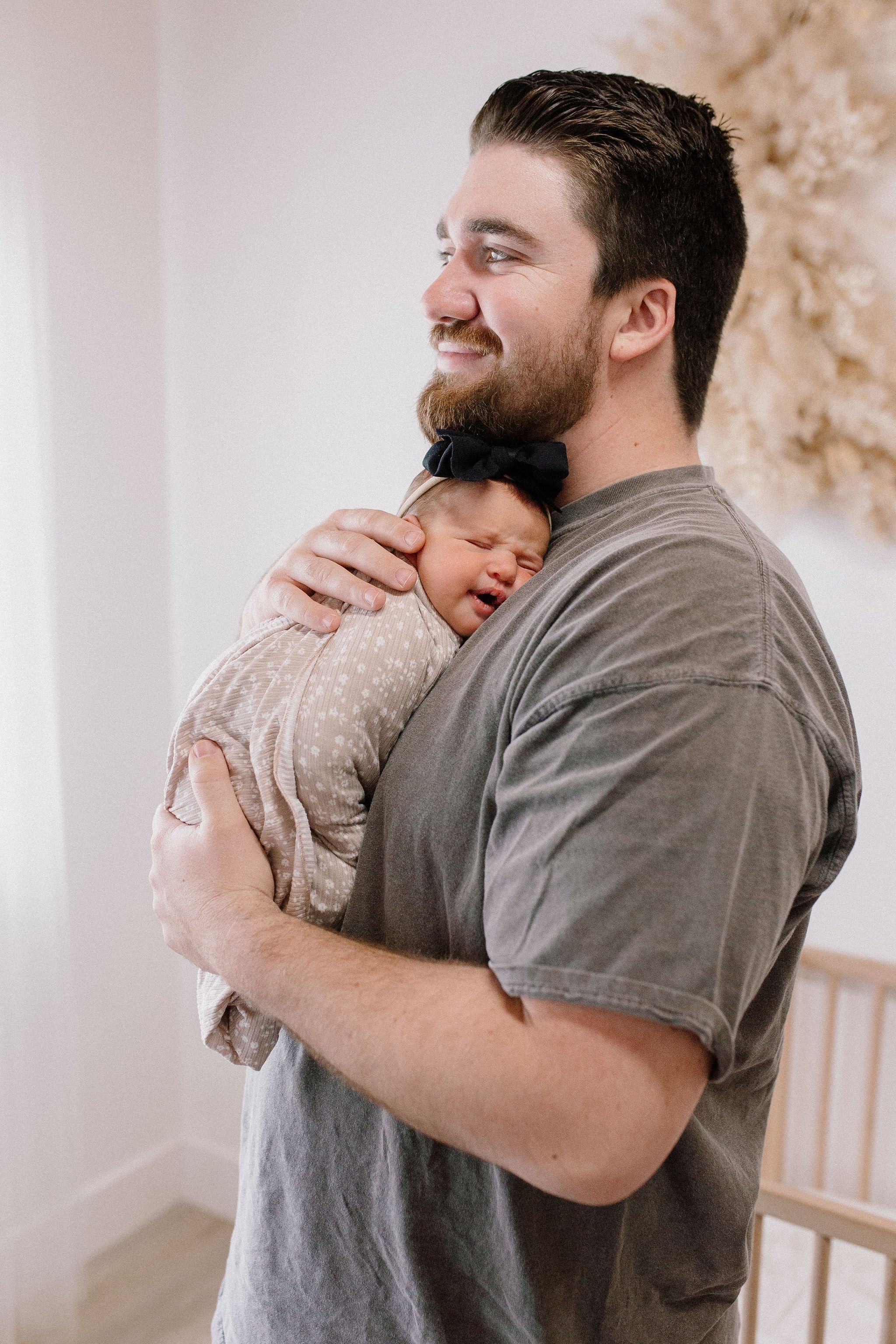 dad holding swaddled newborn baby girl in neutral nursery