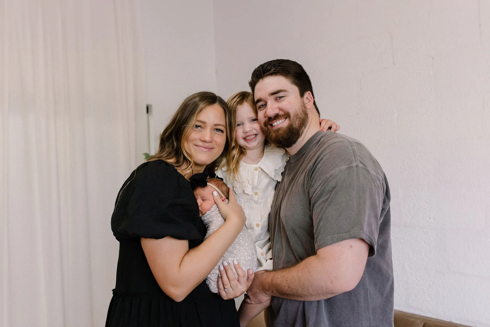 Mom and dad holding newborn baby and toddler in neutral nursery