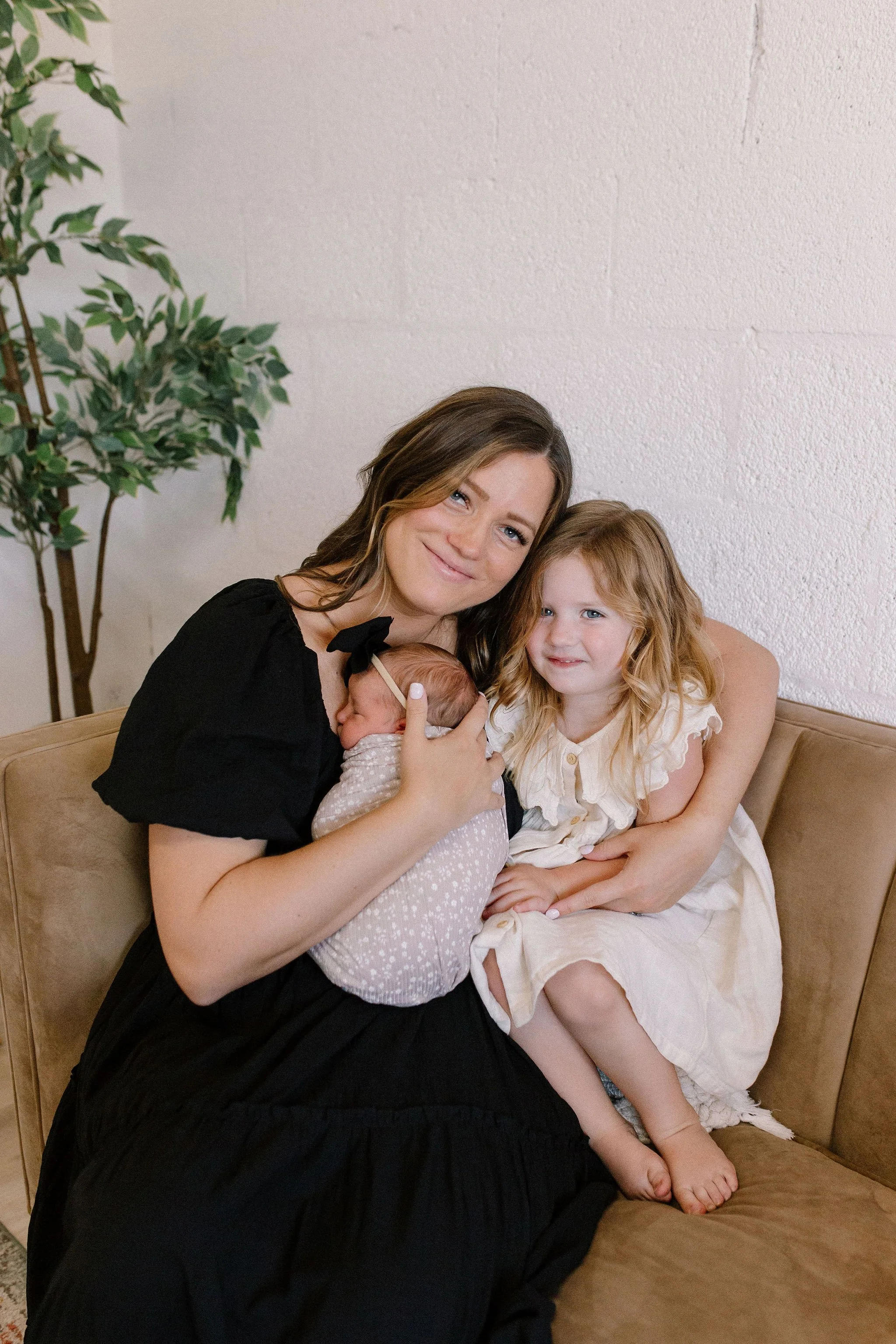 mom and her girls newborn baby and toddler cuddled close on couch in neutral nursery