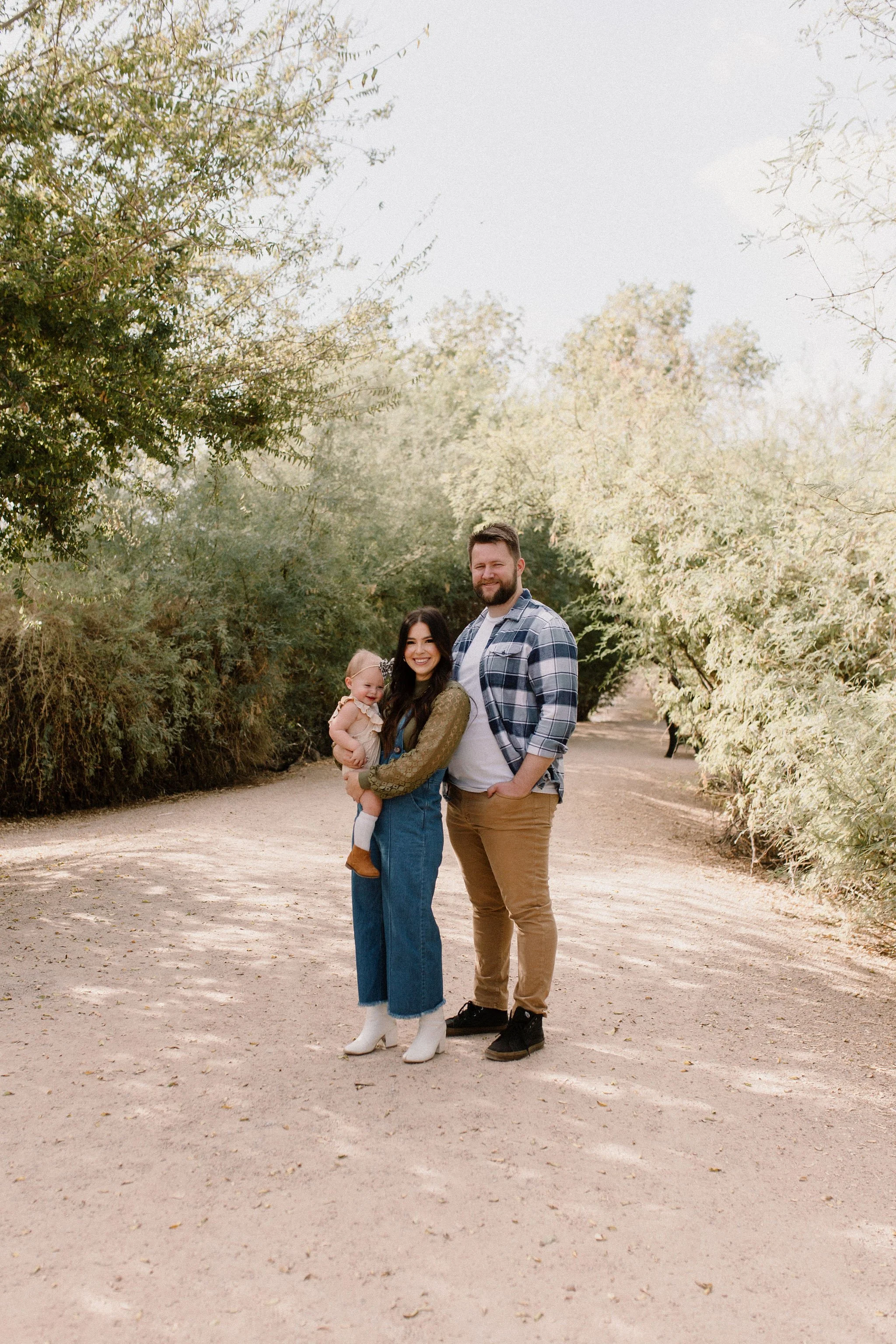 family of three standing together smiling in desert greenery during morning family photography session