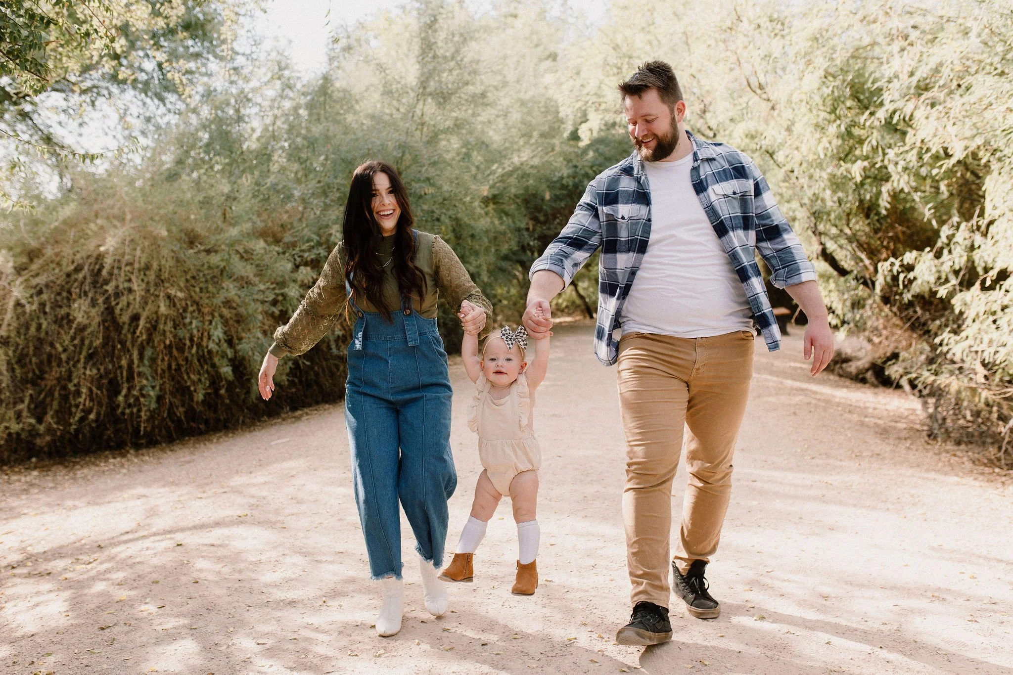 mom and dad walking and swinging toddler in the air in desert greenery family photography session