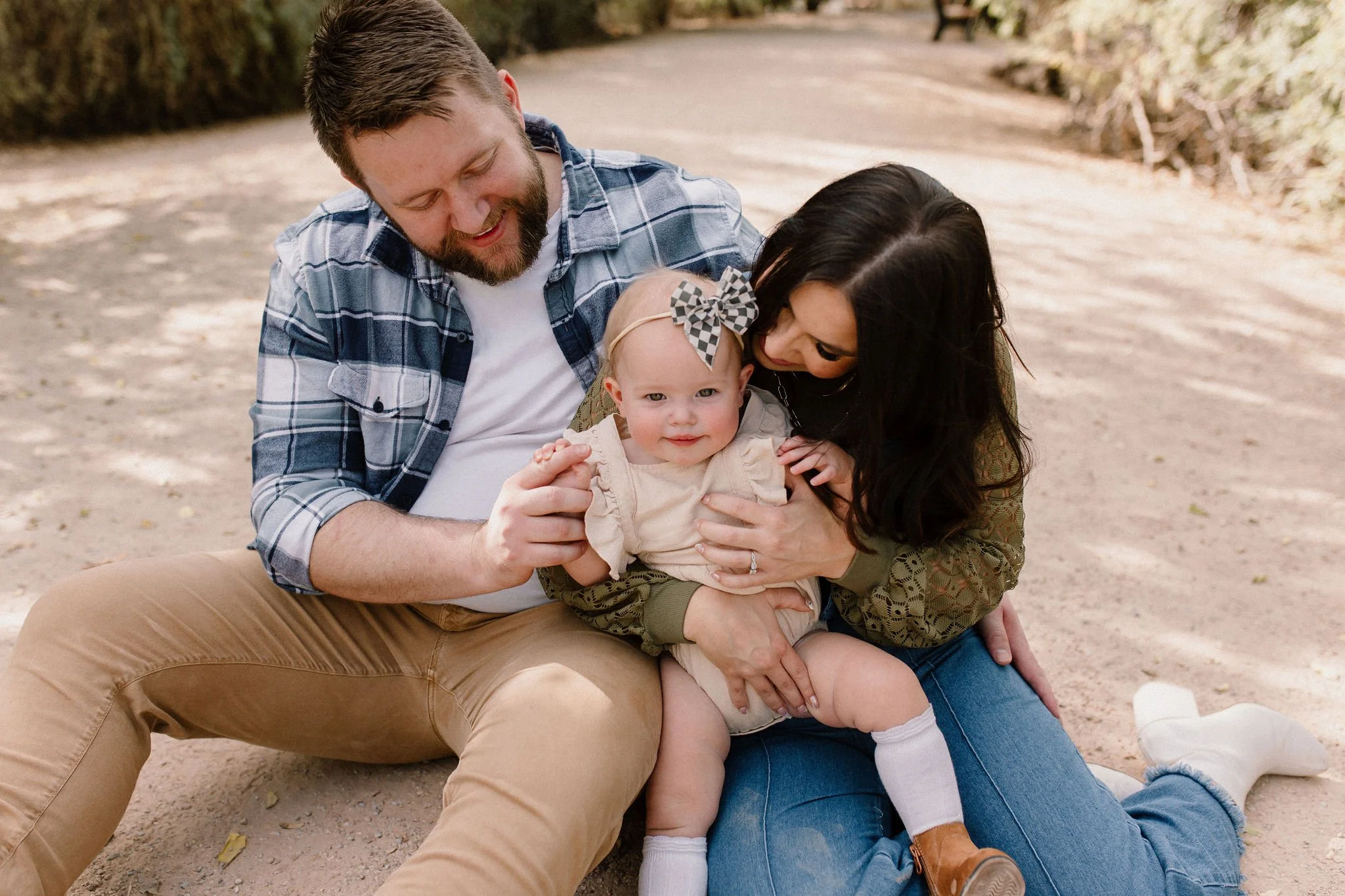 mom and dad playing with baby girl sitting on the ground in desert greenery family photography session