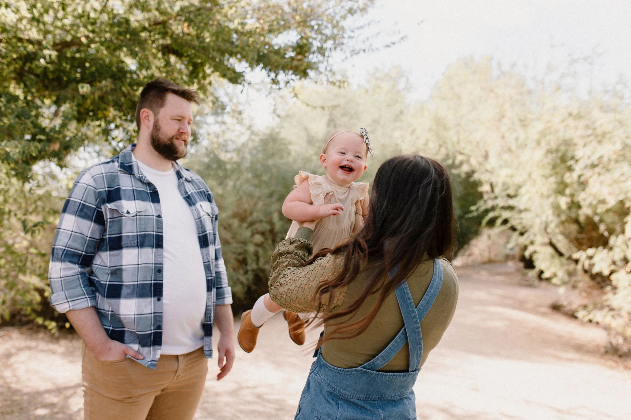 mom spinning baby girl around while dad smiles at them in desert greenery family session