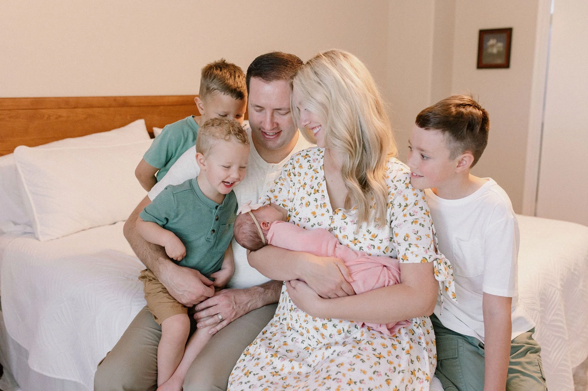 mom holding swaddled newborn baby girl with family surrounding them during lifestyle in-home newborn photography session