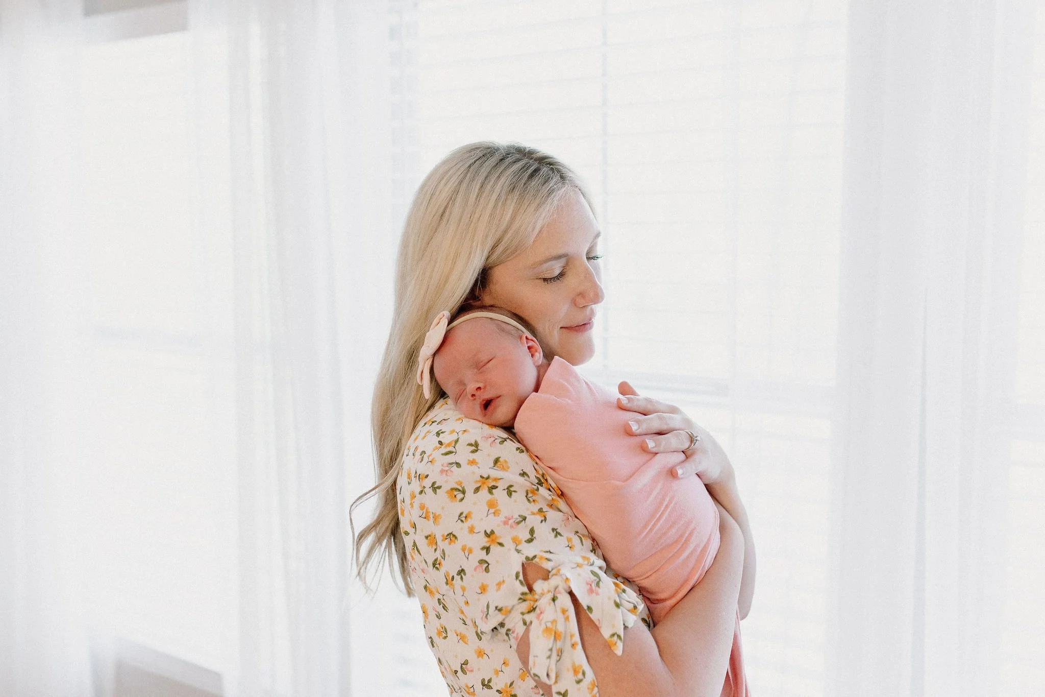 Mom holding baby girl in front of sunny window in-home newborn photography Gilbert, Arizona