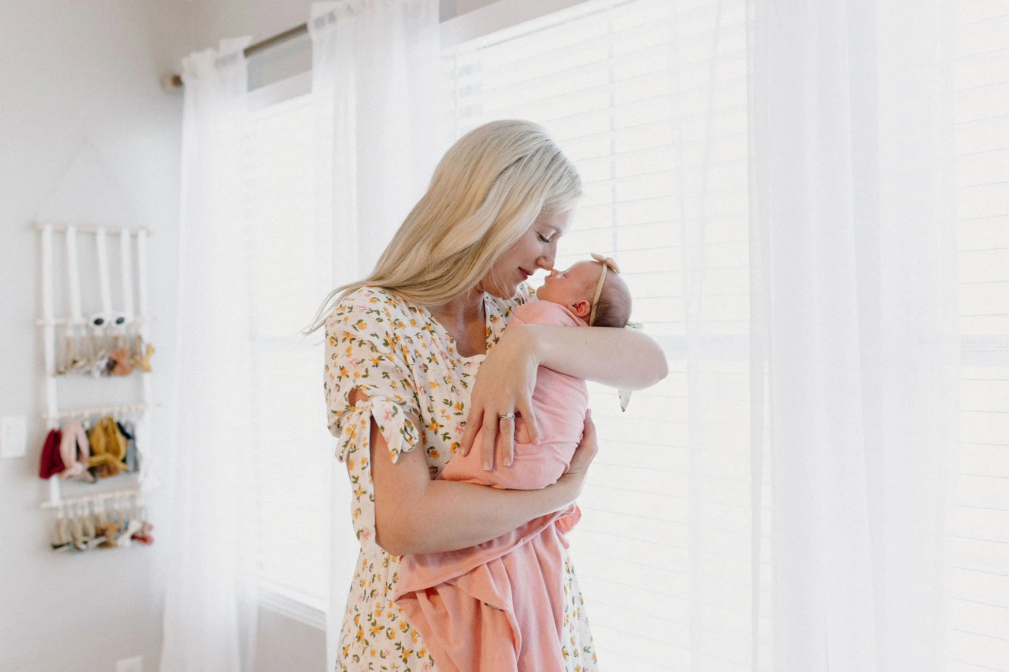 mom holding swaddled newborn baby girl with noses touching in front of windows during lifestyle in-home photography session
