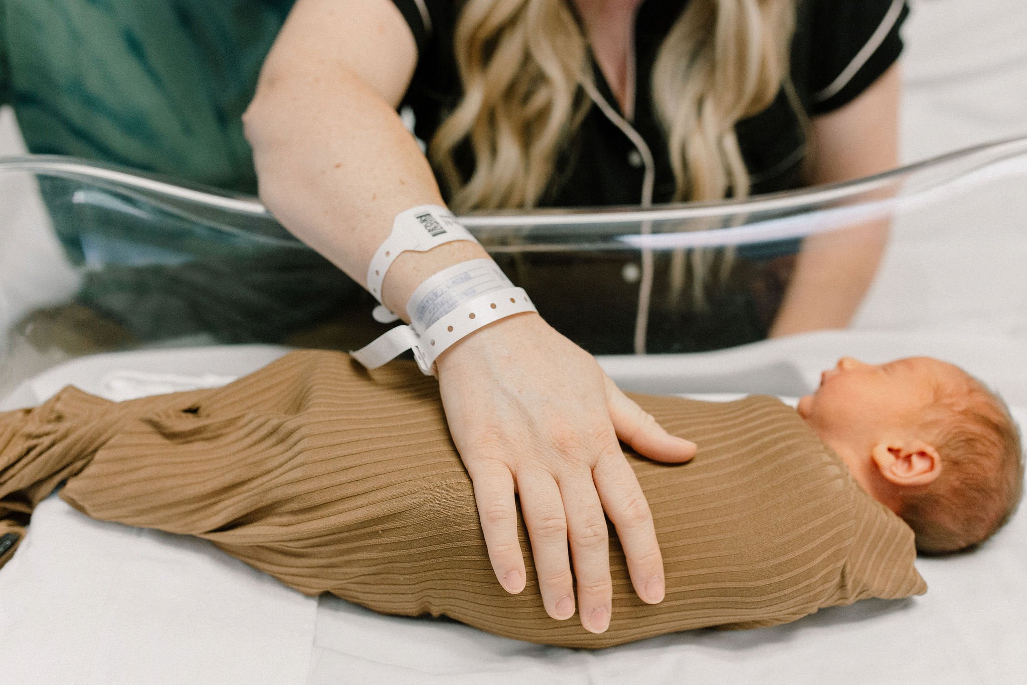 mom patting swaddled newborn baby boy to sleep in hospital bassinet
