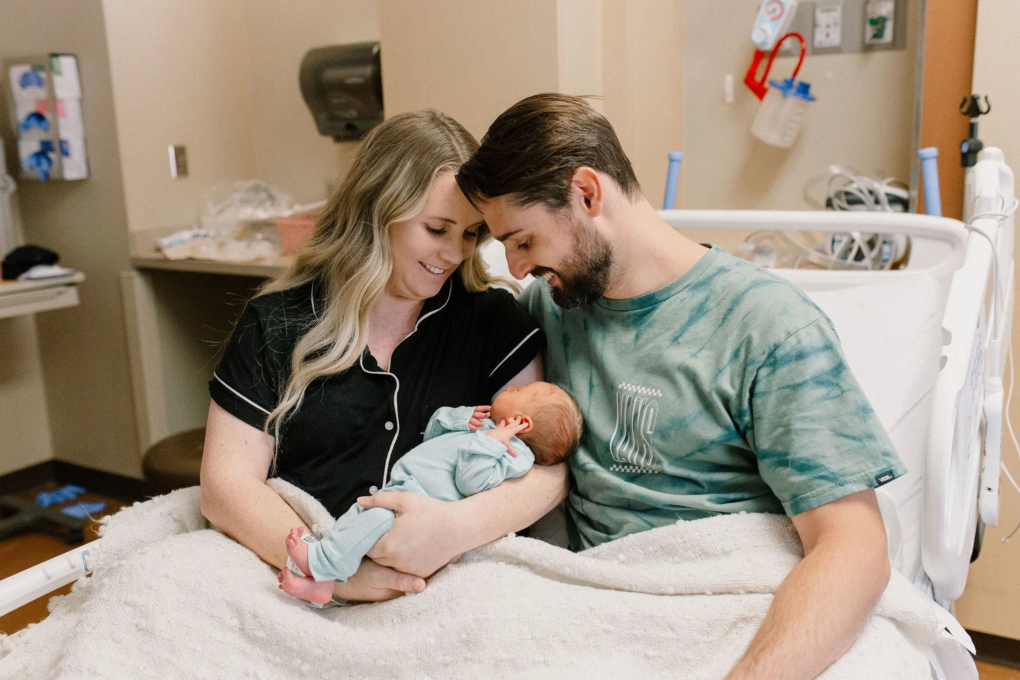 mom and dad sitting in hospital bed holding and looking at newborn baby boy after birth
