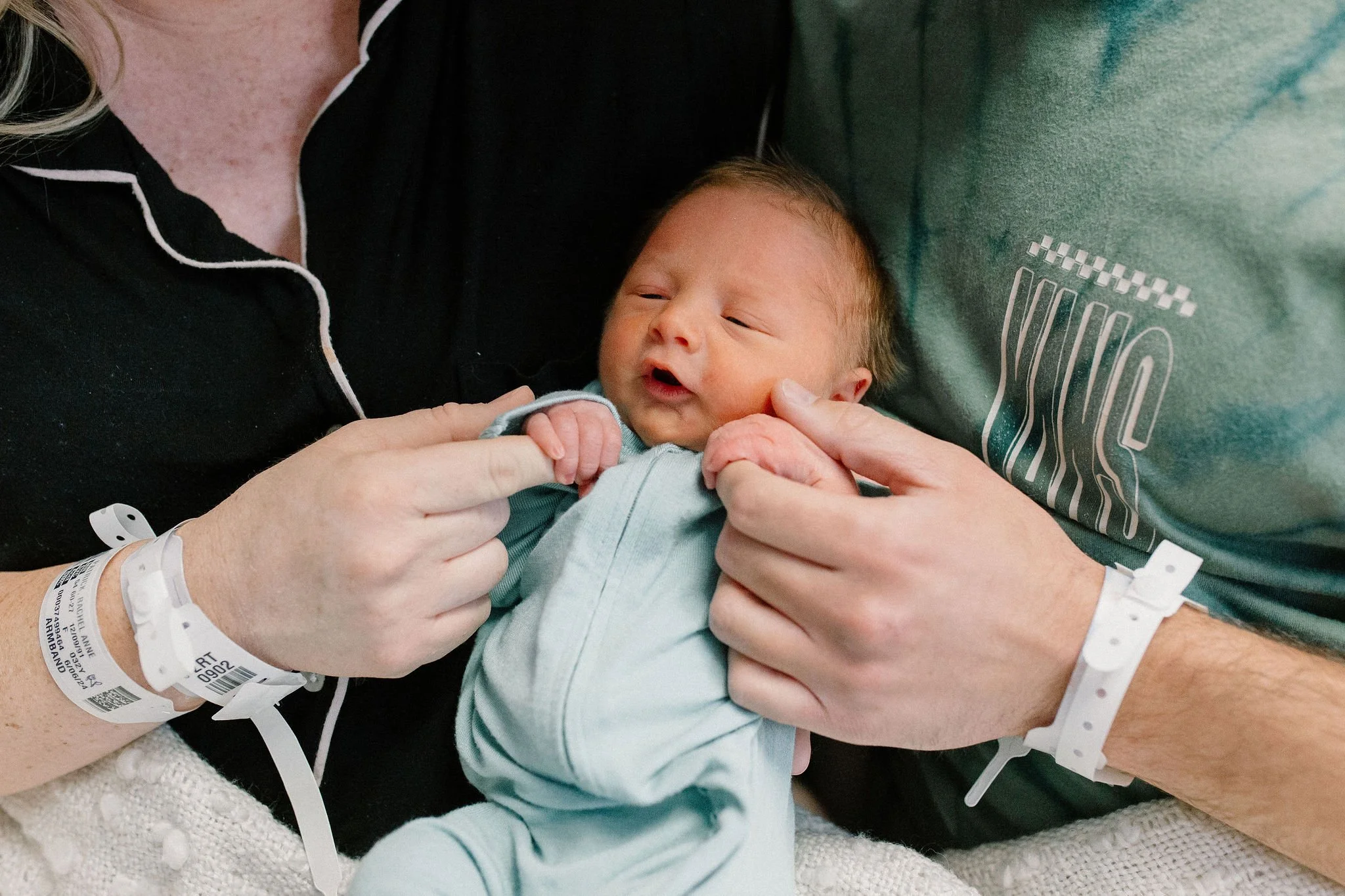 newborn baby holding mom and dad's fingers in hospital room after birth