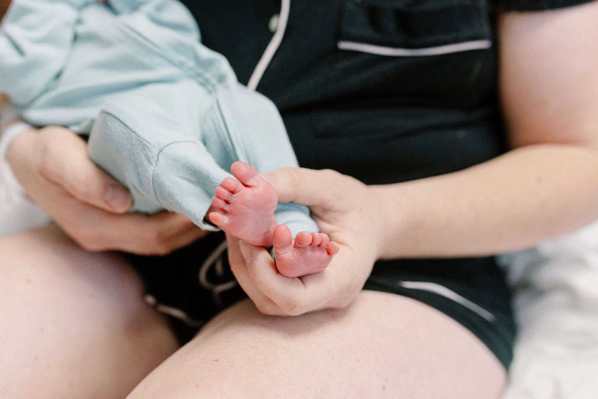 mom holding newborn baby boy's feet in hospital room after birth