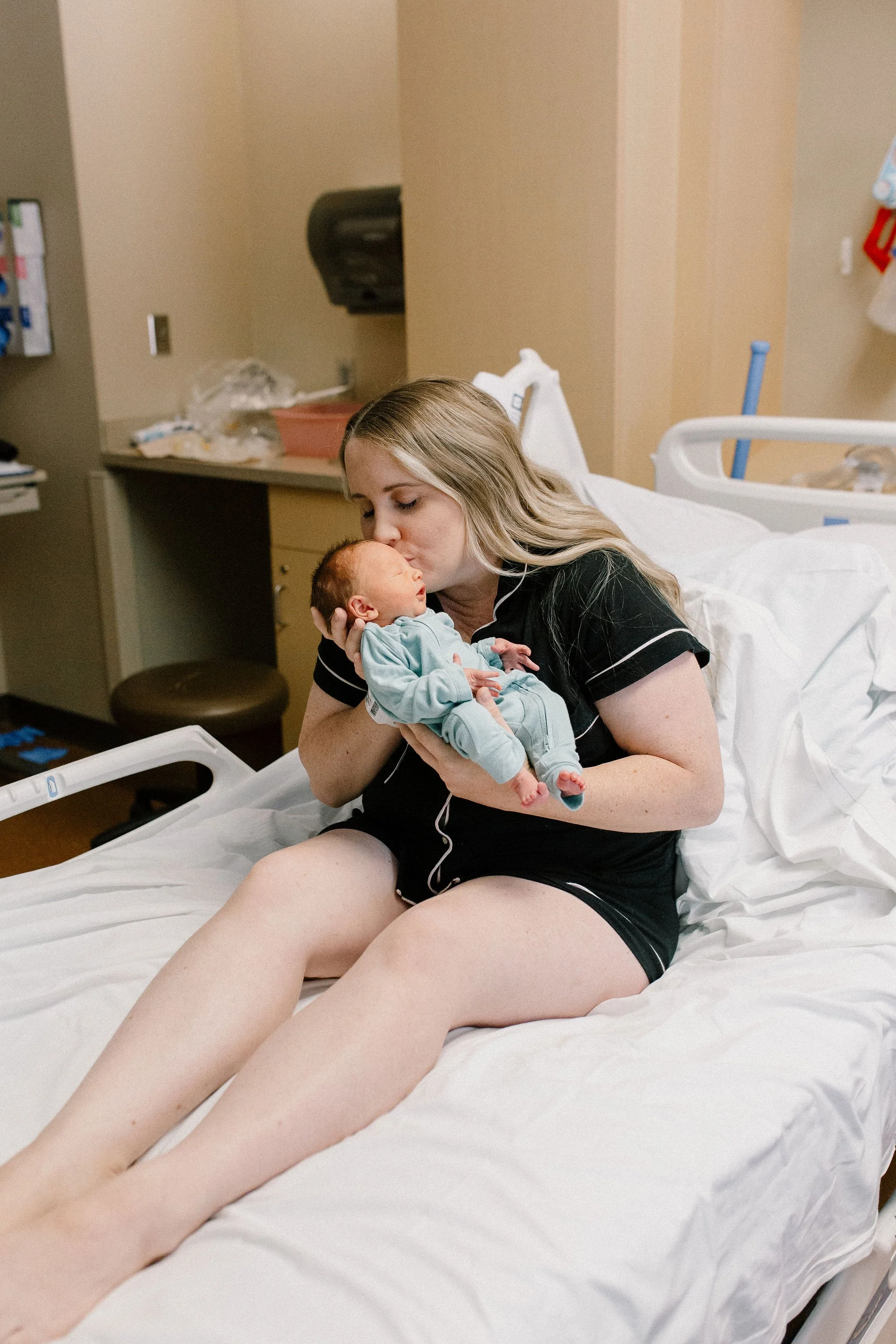 mom holding and kissing newborn baby boy in hospital bed after birth