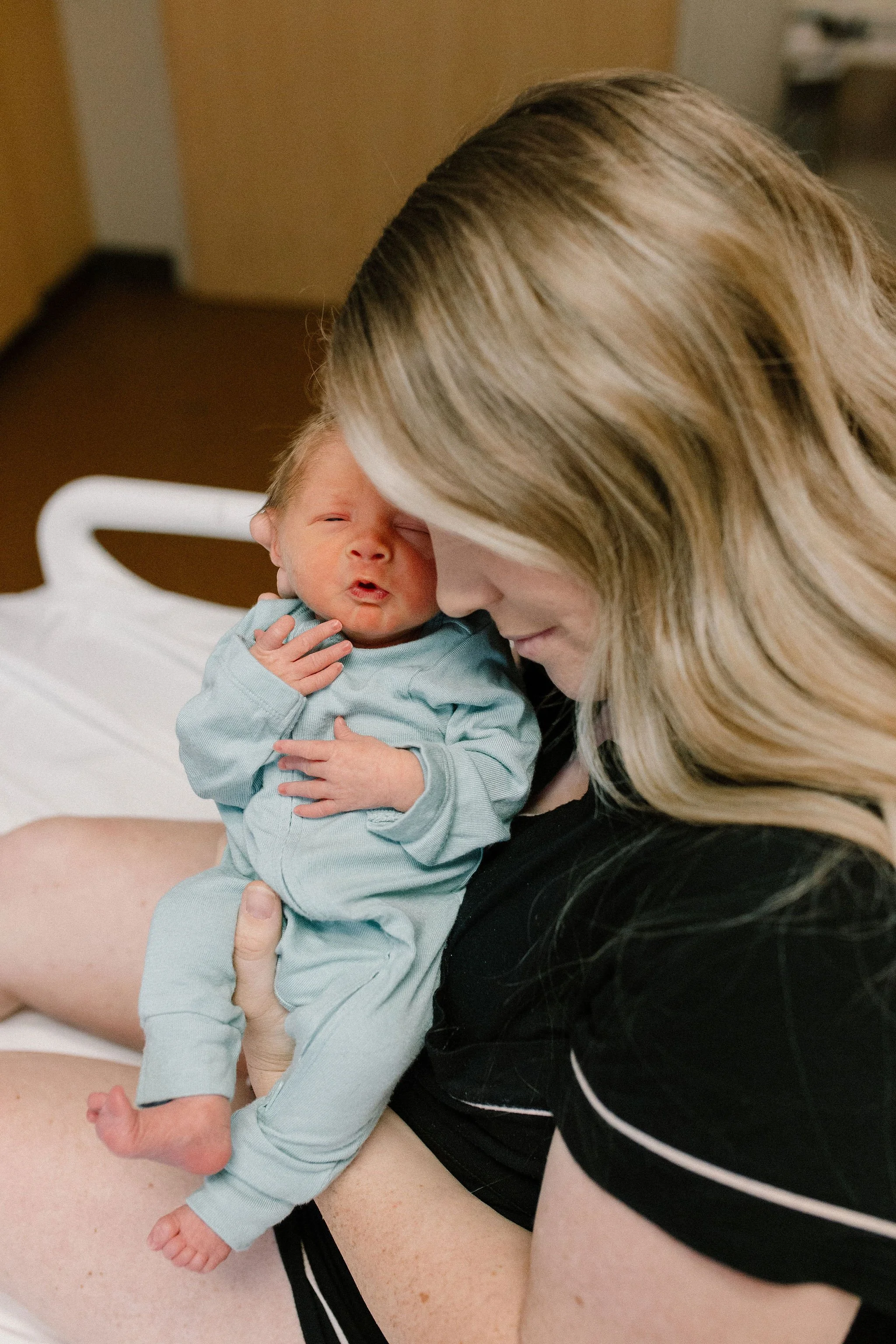mom holding newborn baby boy in hospital bed after birth