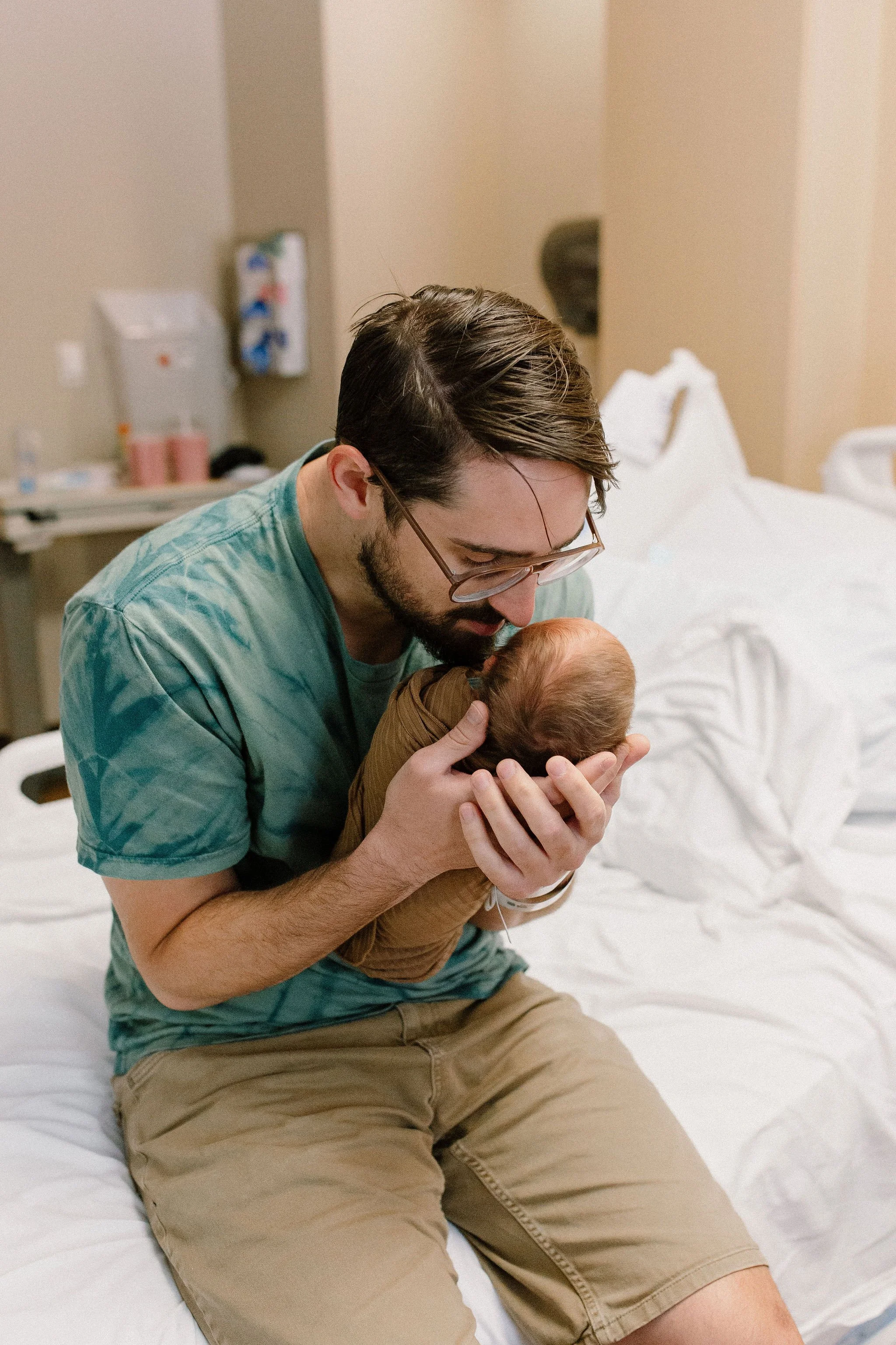 dad holding newborn baby boy in hospital bed after birth