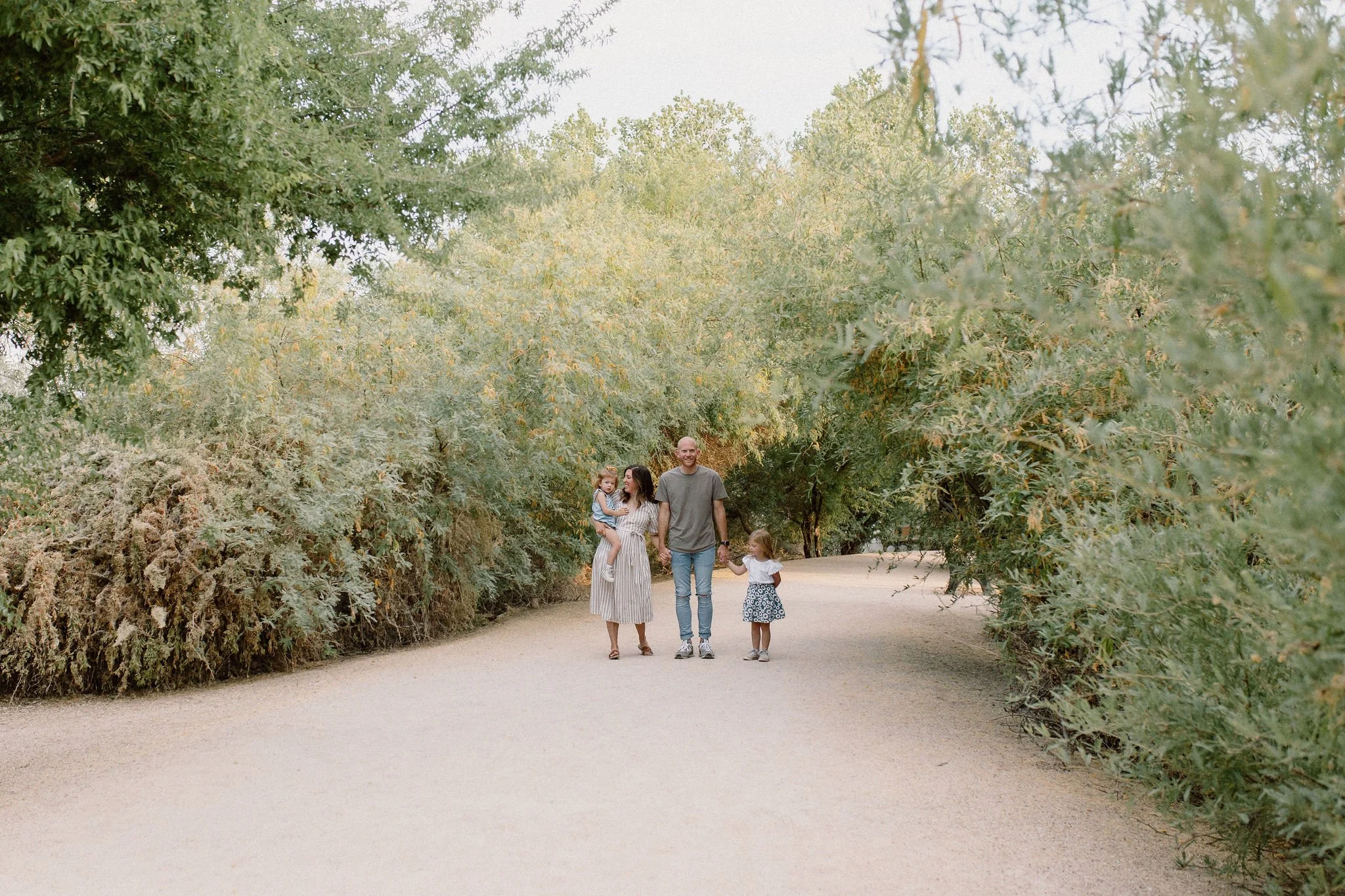 family of four walking together holding hands in desert greenery family photography session
