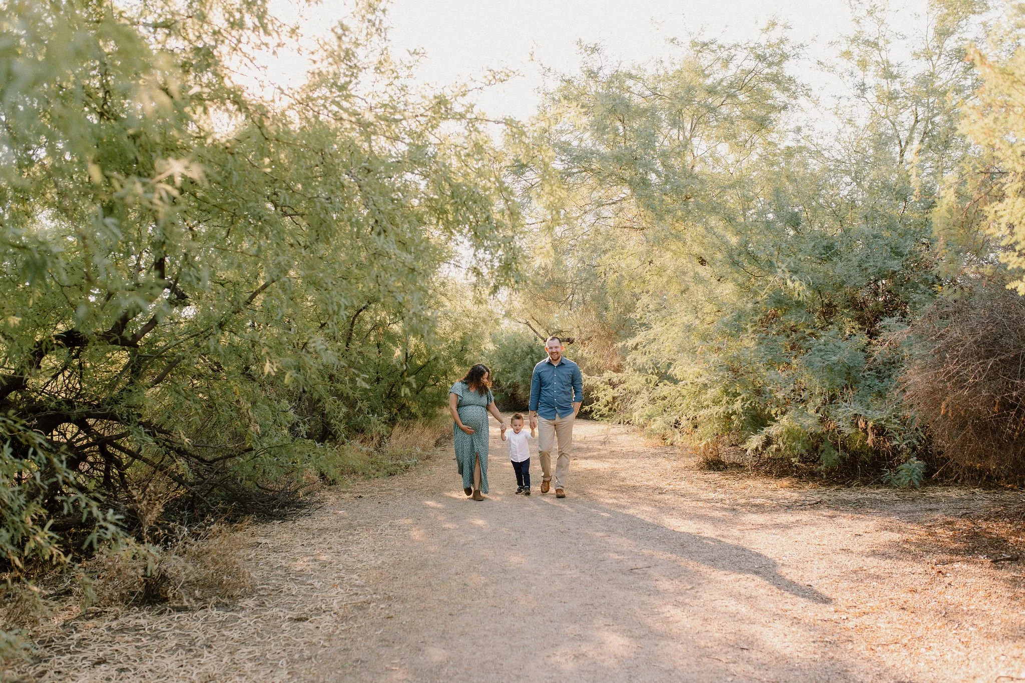 family holding hands and walking in desert greenery during maternity photography session