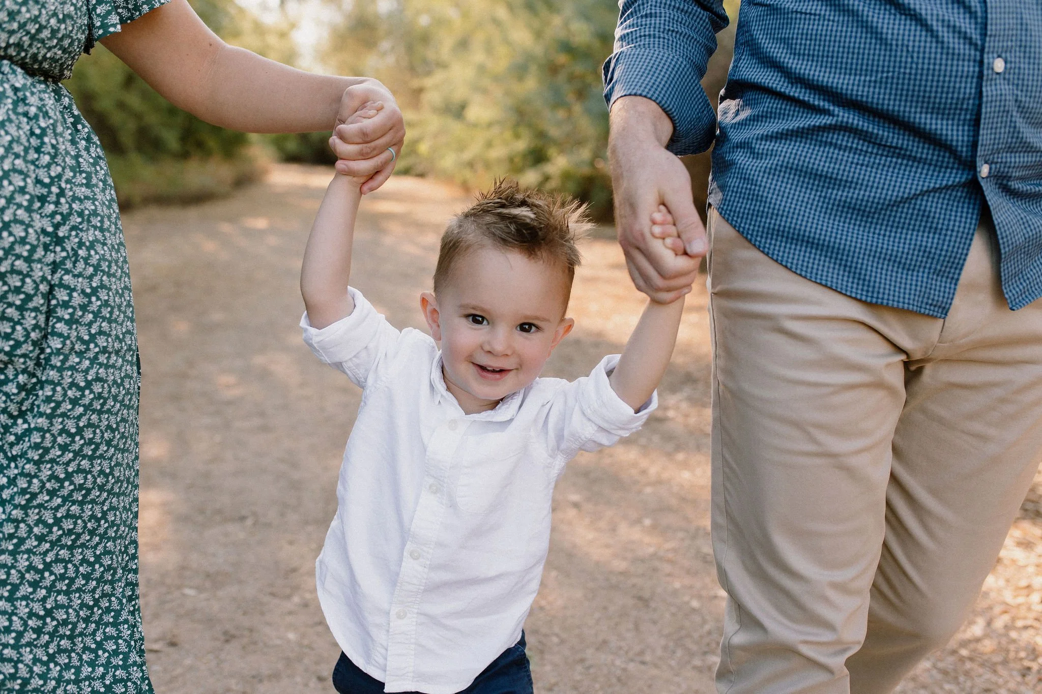 toddler walking holding mom and dad's hand during family maternity photography session