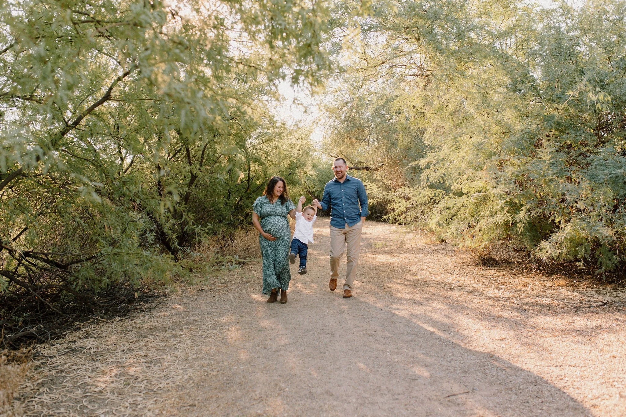 family walking and holding hands and swinging toddler in the air during maternity photography session