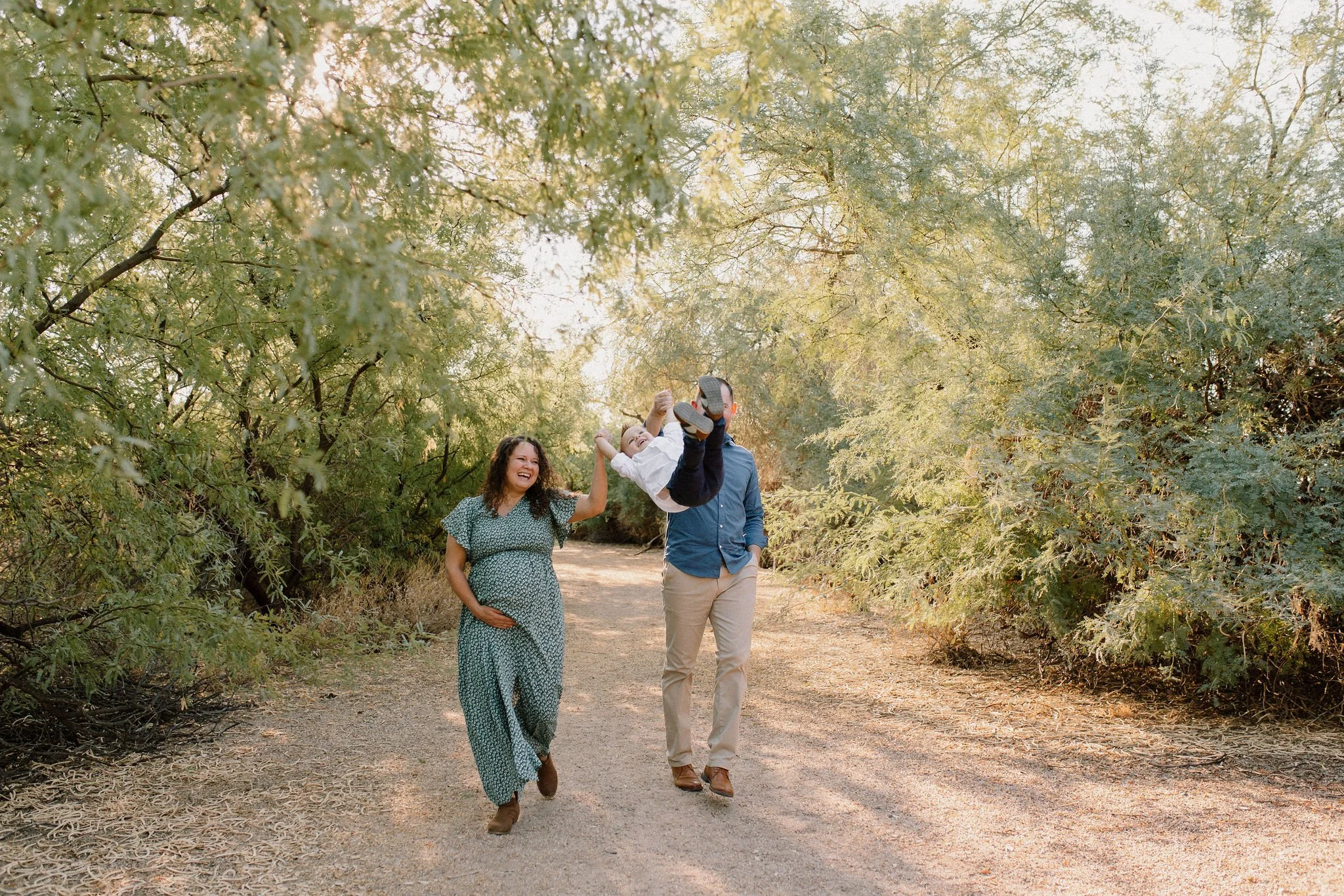 family walking and holding hands and swinging toddler in the air during maternity photography session