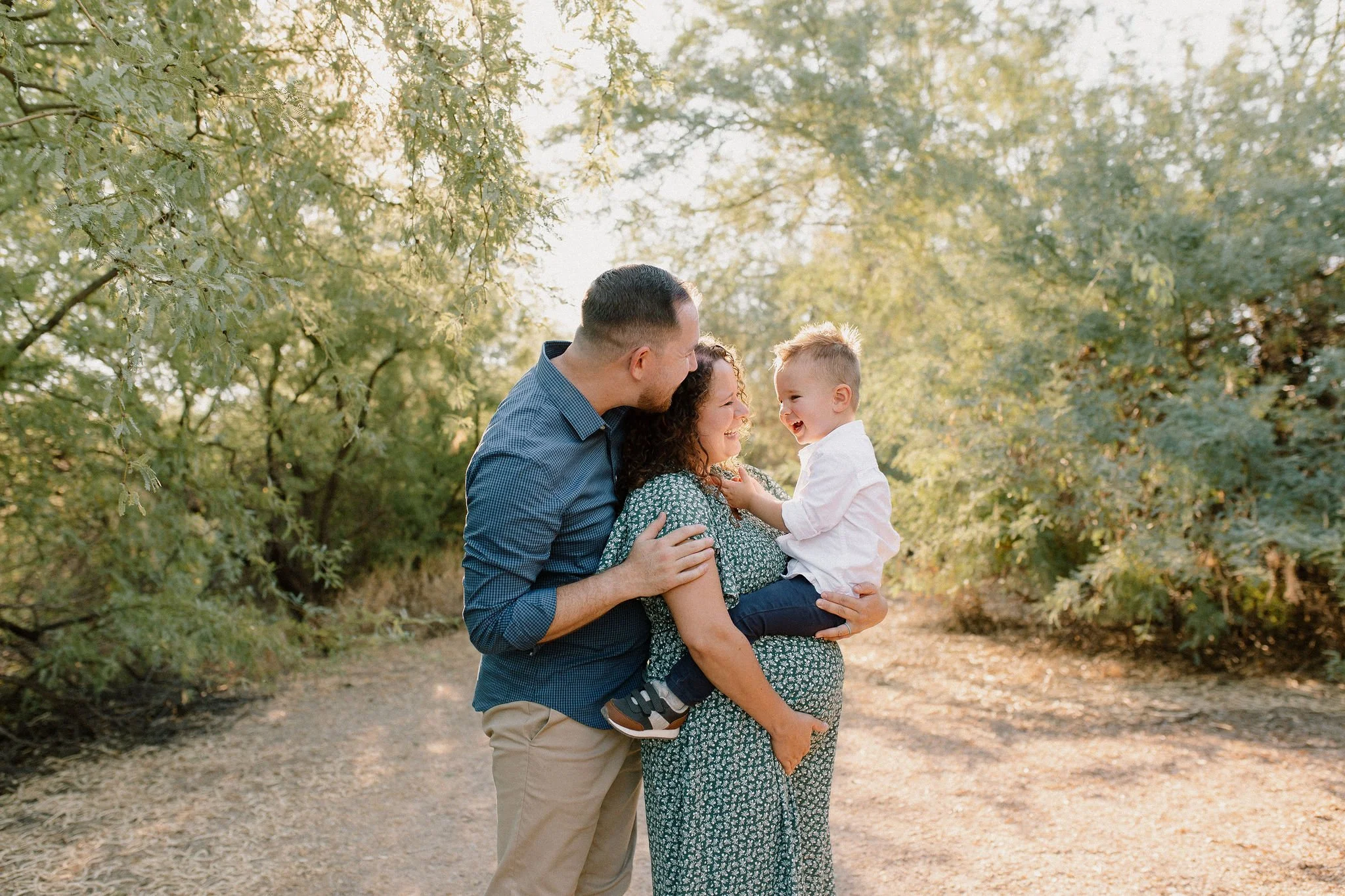 toddler sitting on pregnant mom's belly smiling and laughing at mom and dad during family maternity photography session