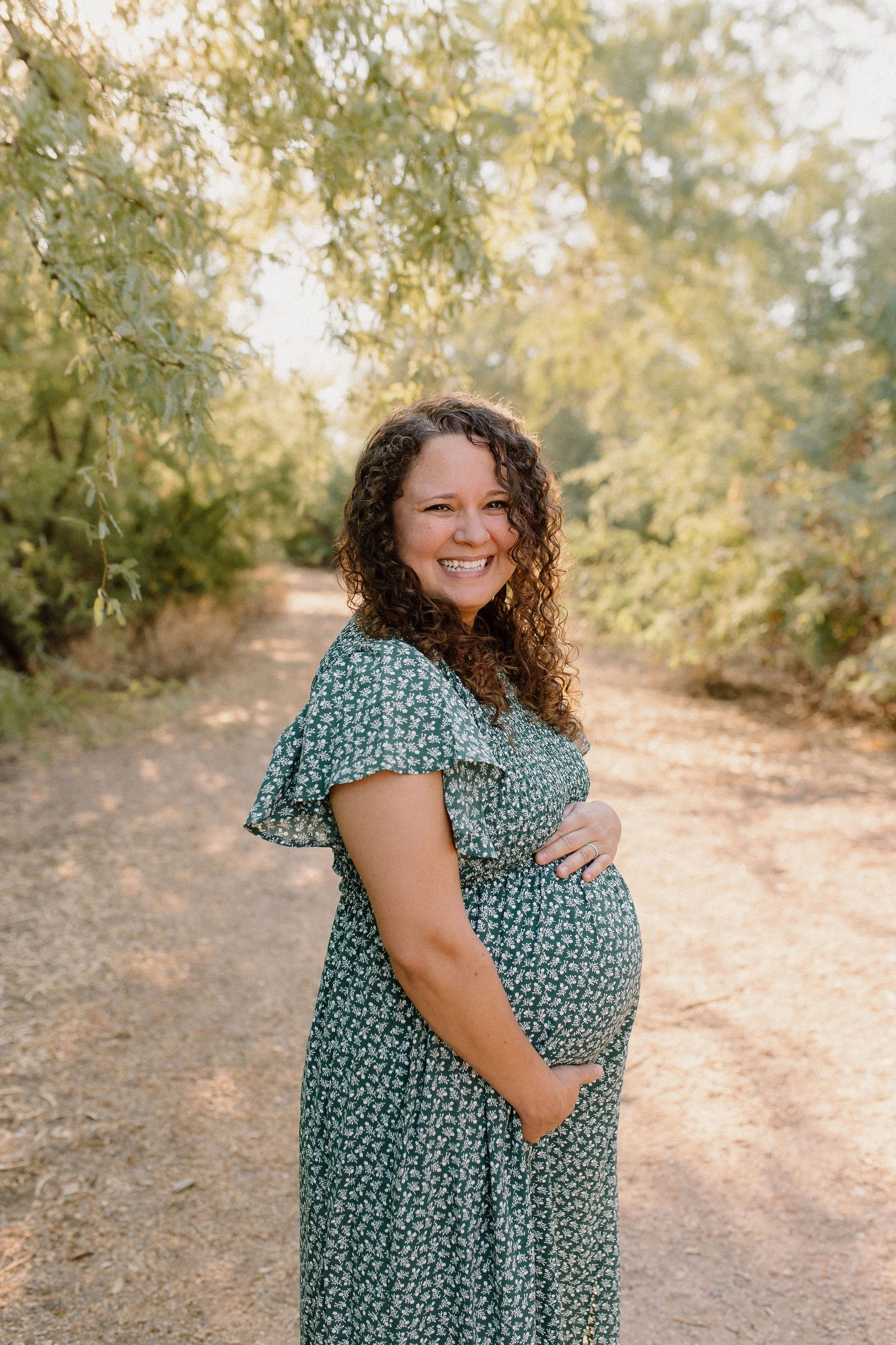 portrait of pregnant mom in desert greenery with ditsy floral dress during family maternity photography session at Gilbert Riparian Preserve in Arizona