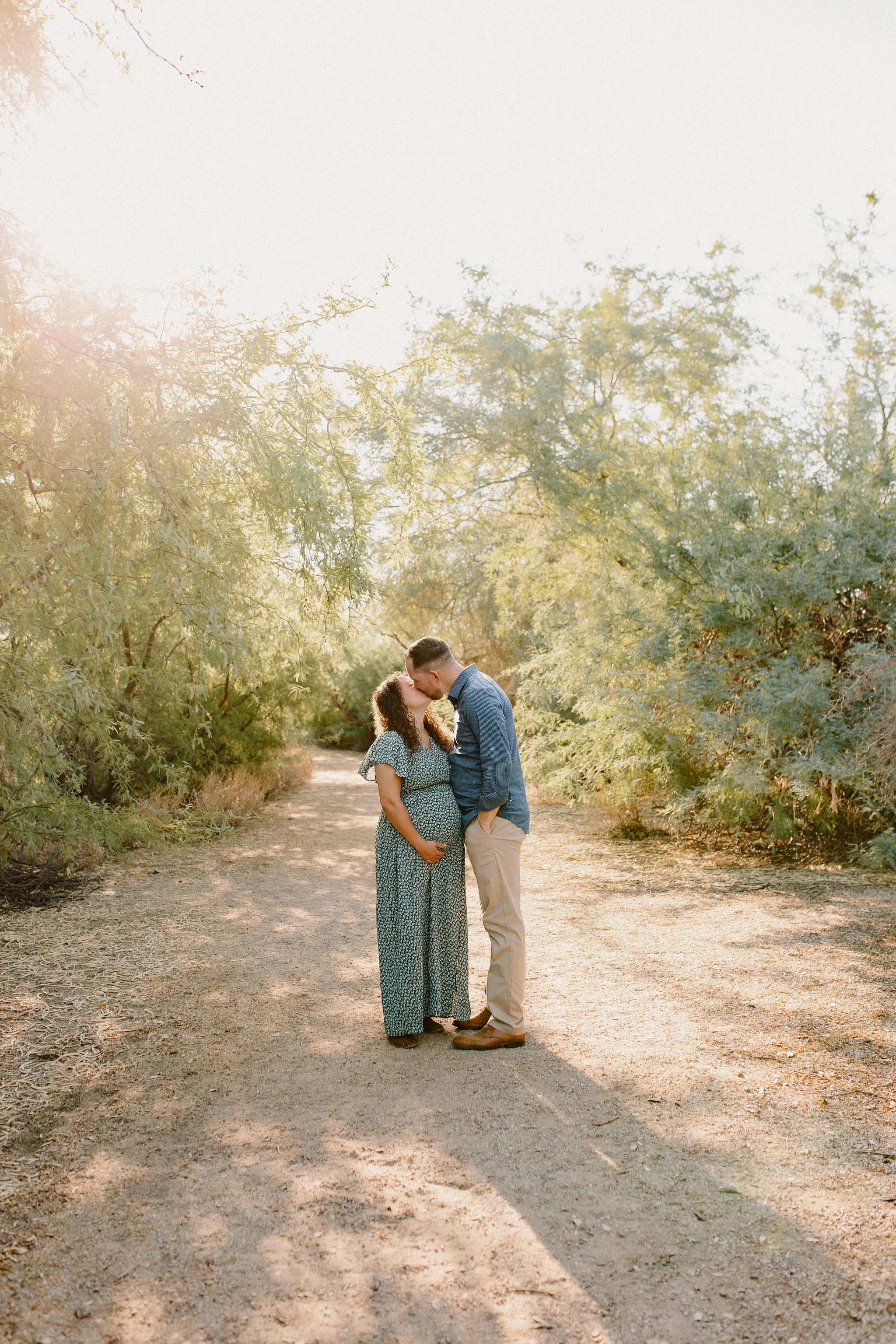 pregnant mom and dad standing close and smiling at each other in desert greenery maternity photos