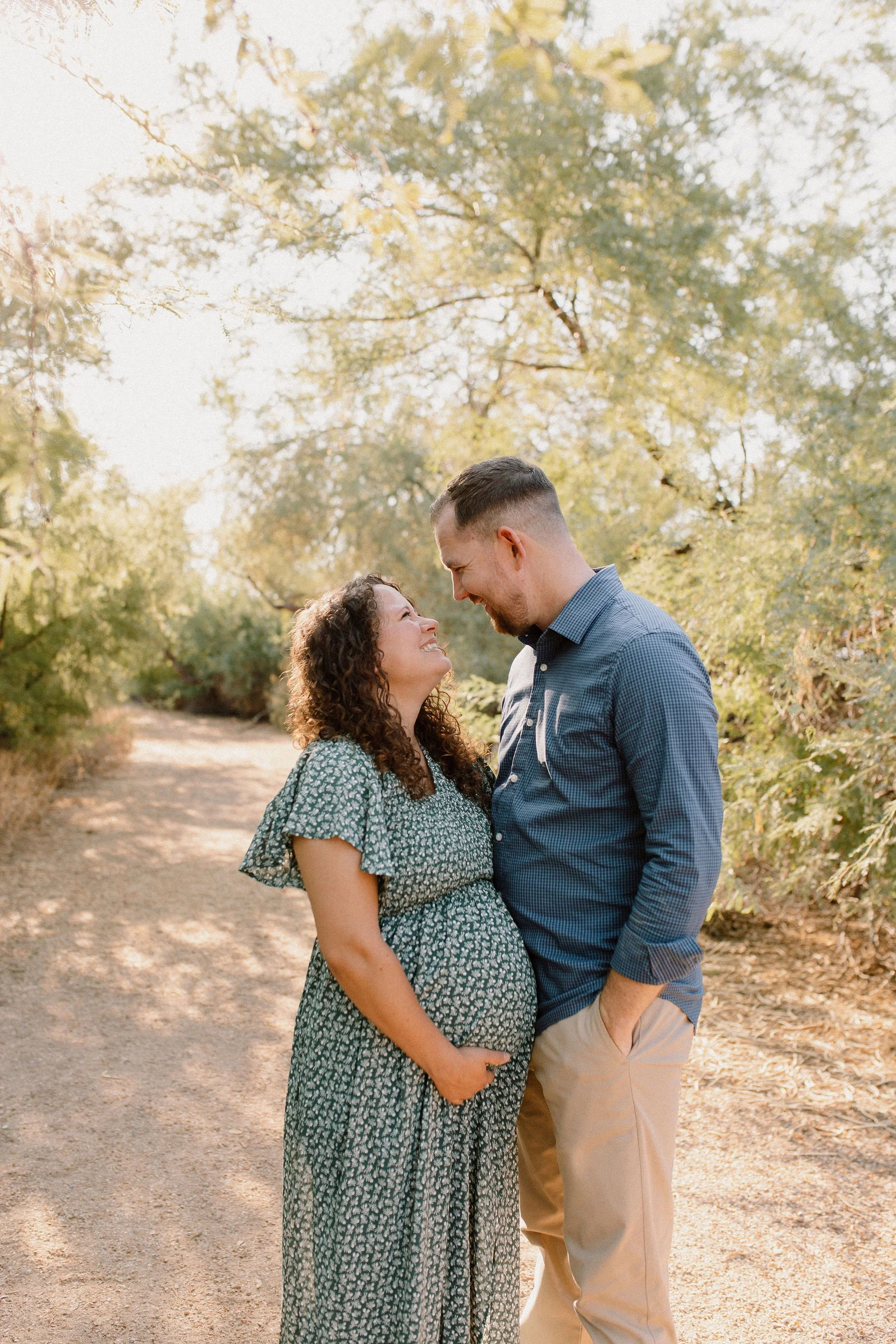 pregnant mom and dad standing close and smiling at each other in desert greenery maternity photos
