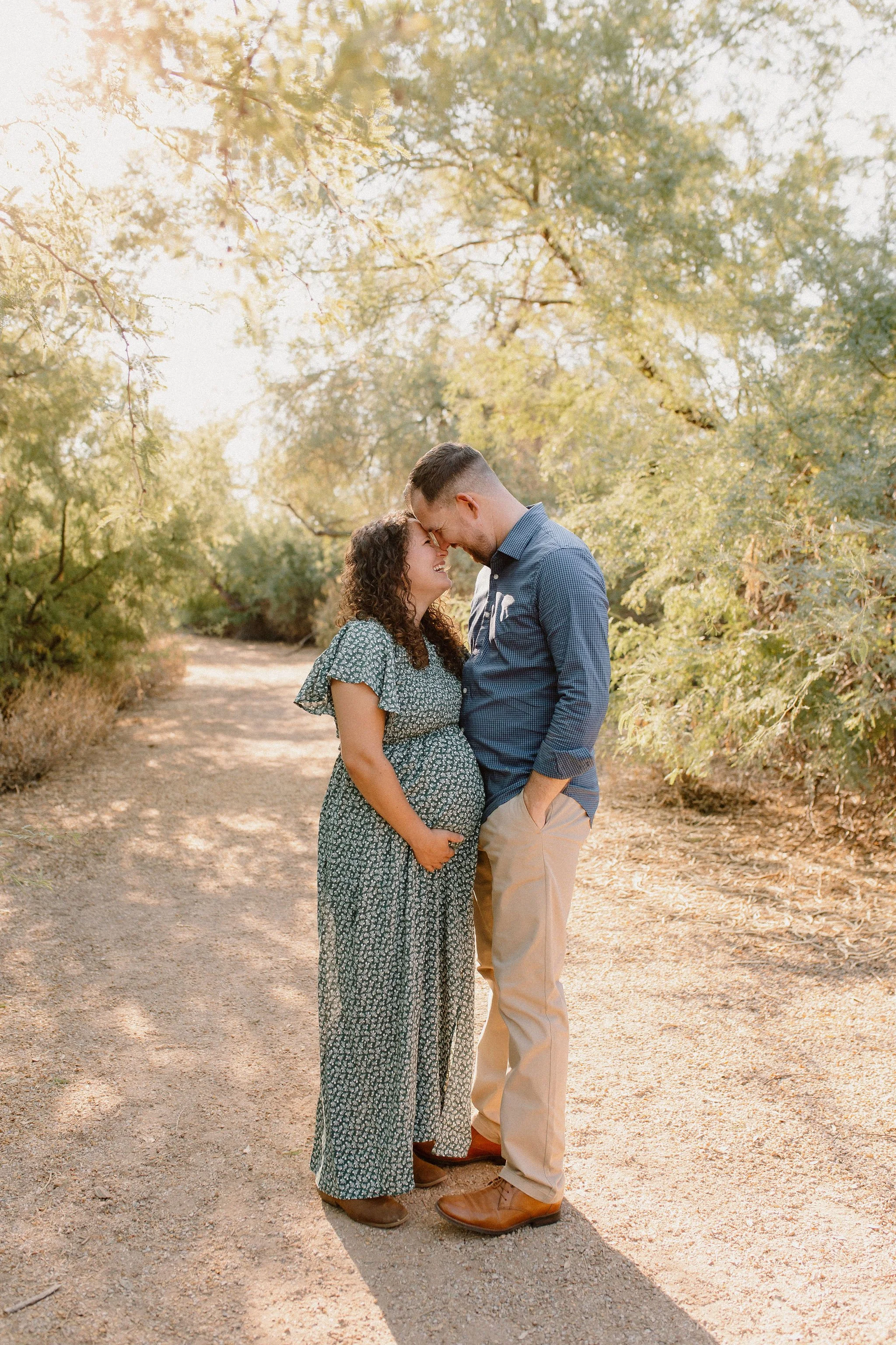 pregnant mom and dad standing close and smiling at each other in desert greenery maternity photos