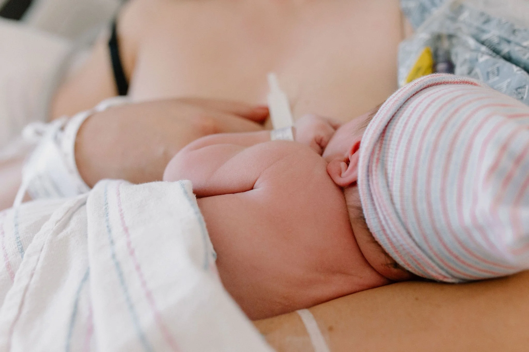 close up of newborn baby cuddled up to mom after birth in hospital bed