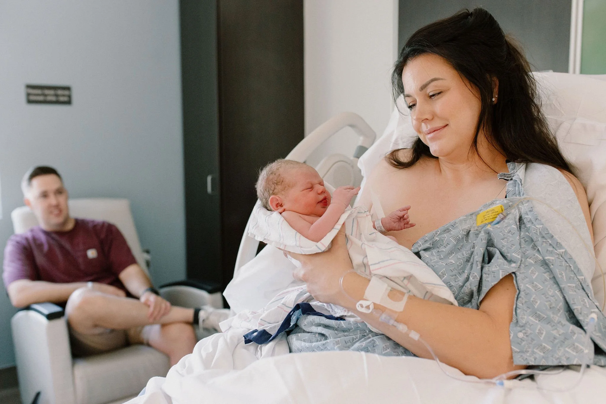 mom and dad smiling at newborn baby girl in hospital after birth