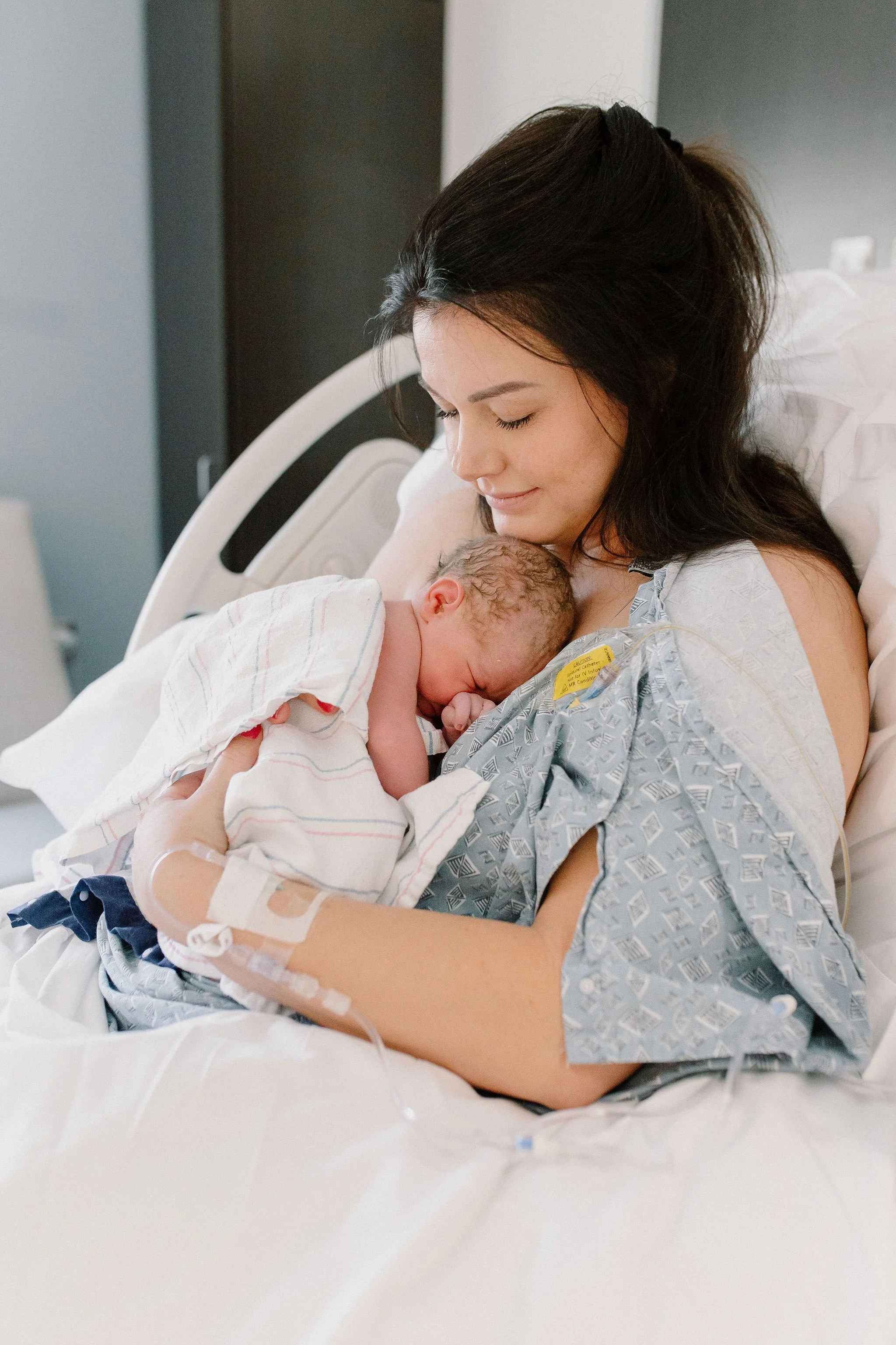 mom holding newborn baby in hospital bed after birth