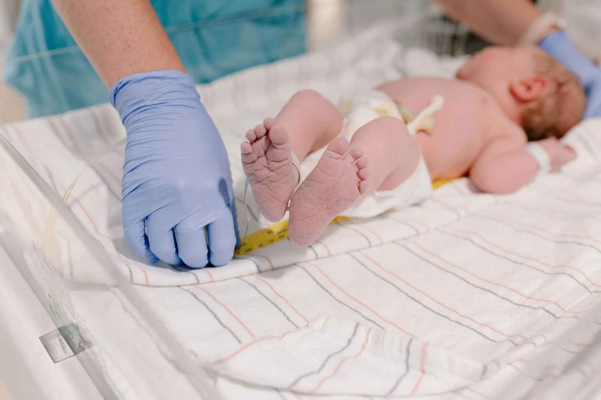 close up detail photo of newborn baby feet and toes being measured in hospital bassinet after birth