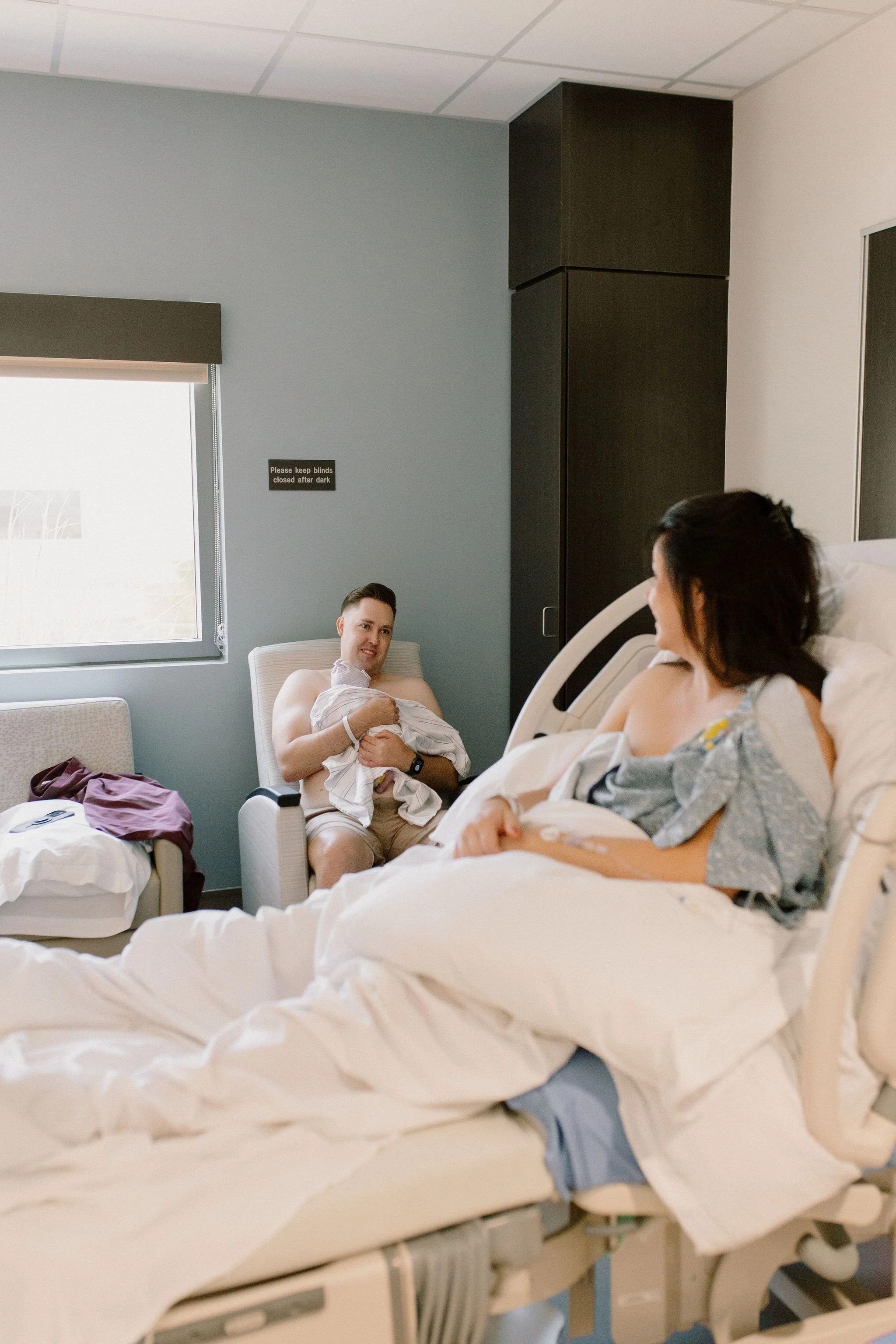mom smiling at dad holding newborn baby girl for the first time in hospital after birth