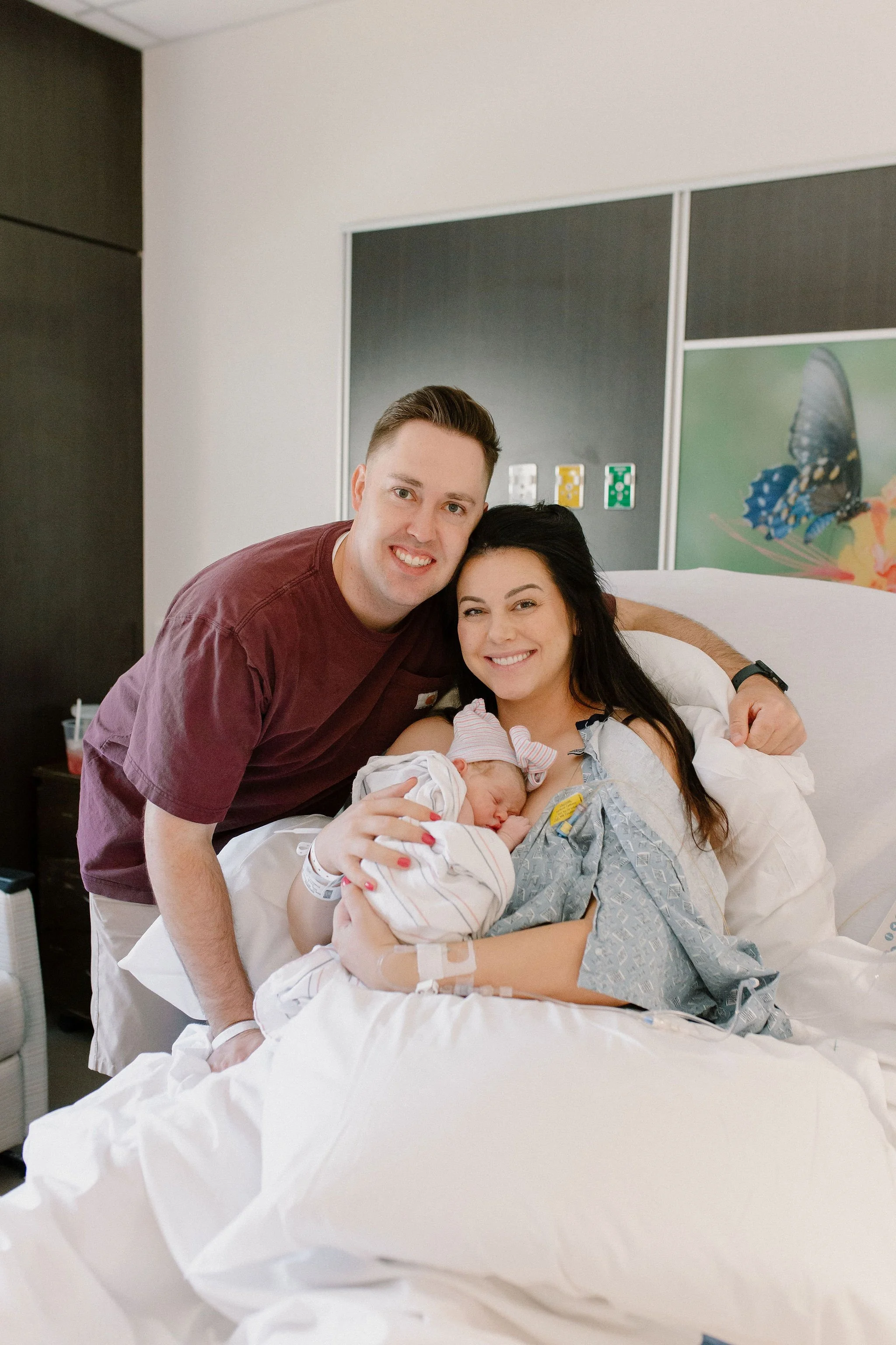 mom and dad smiling holding newborn baby in hospital during birth photography session