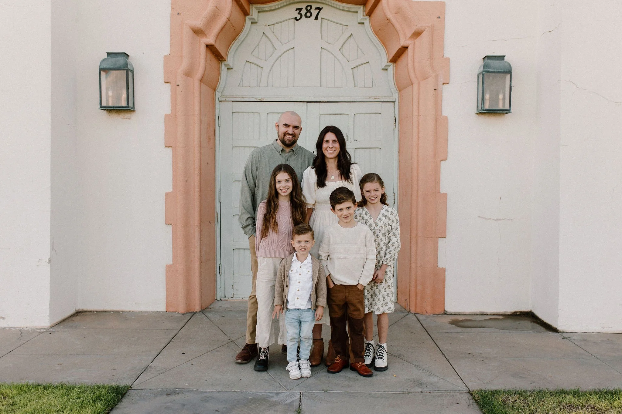 family of six standing together smiling in front of vintage blue and pink door during extended family photography session