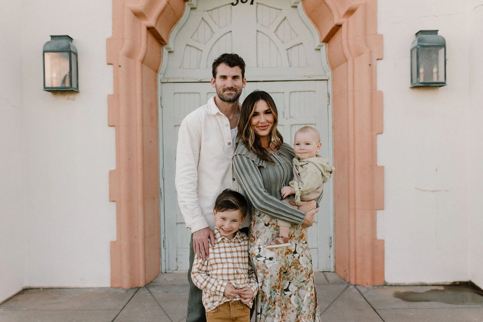 mom and dad holding toddler and baby in front of bougainvilleas during extended family photos