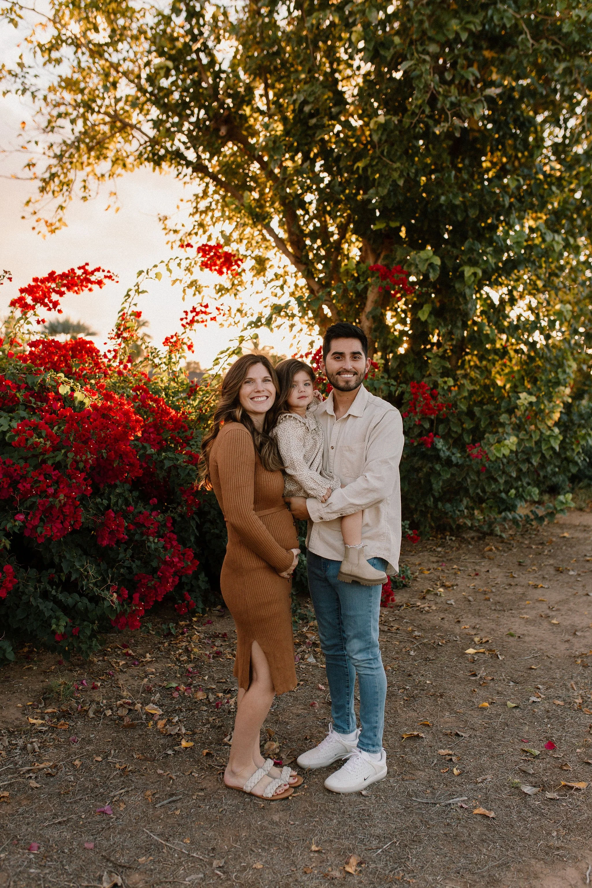 pregnant mom with husband and toddler smiling in front of bougainvilleas during extended family photos