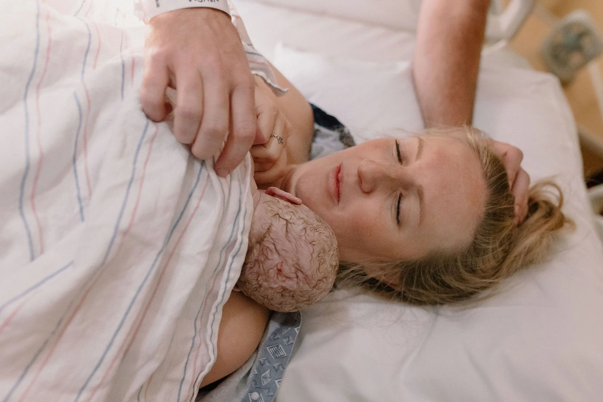 mom holding newborn baby immediately after birth with dad touching them to support