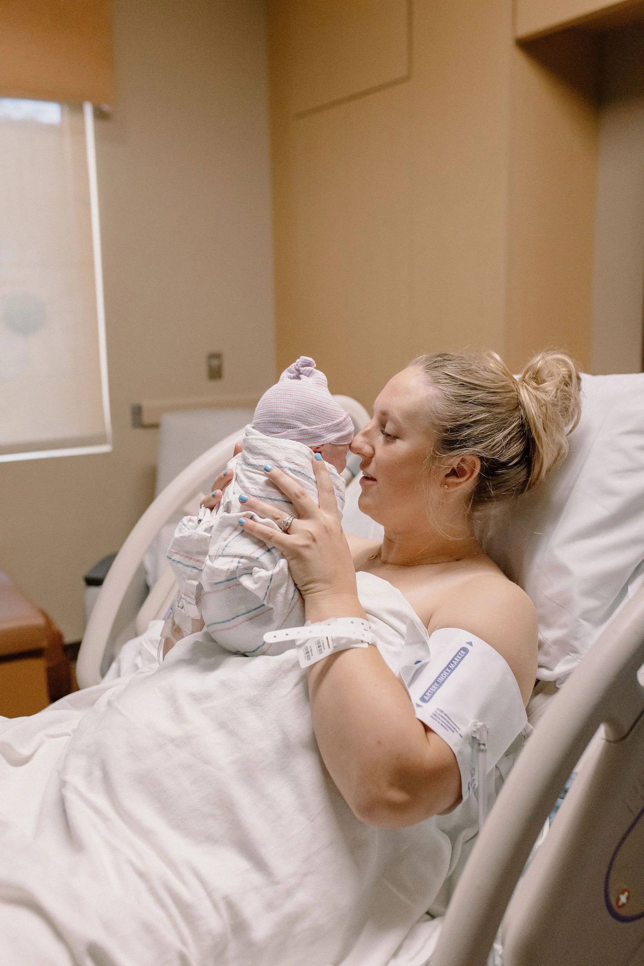 mom holding swaddled newborn baby close to her face in hospital bed after birth