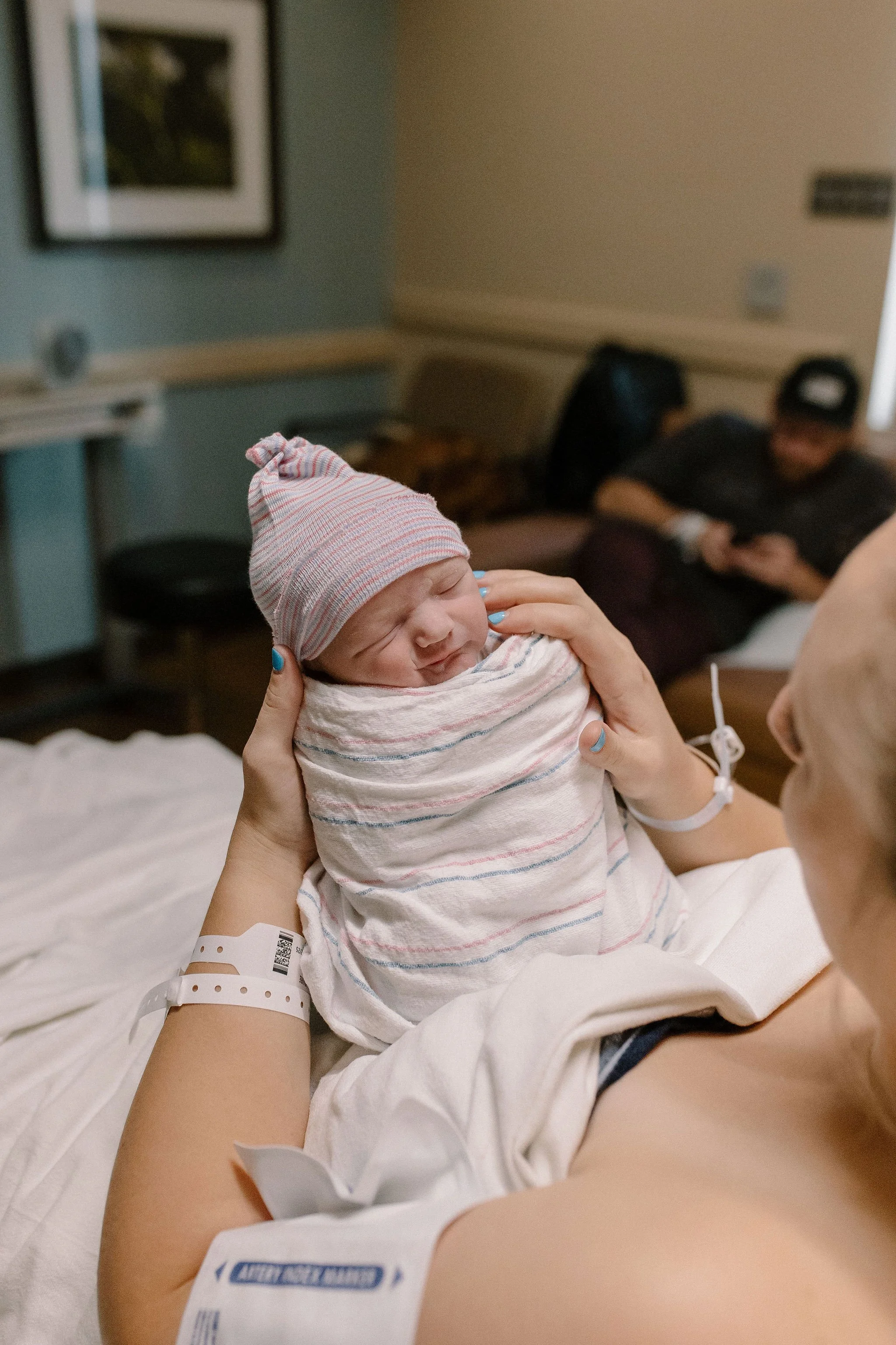 mom holding swaddled newborn baby in hospital room after birth