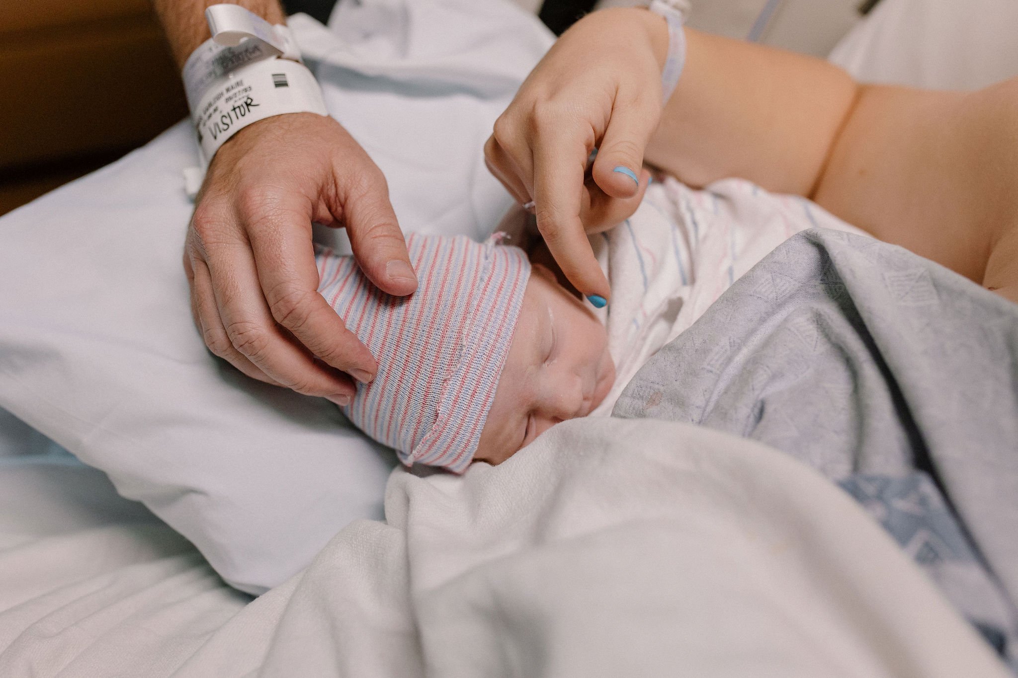 mom and dad's hands touching swaddled newborn baby in hospital after birth