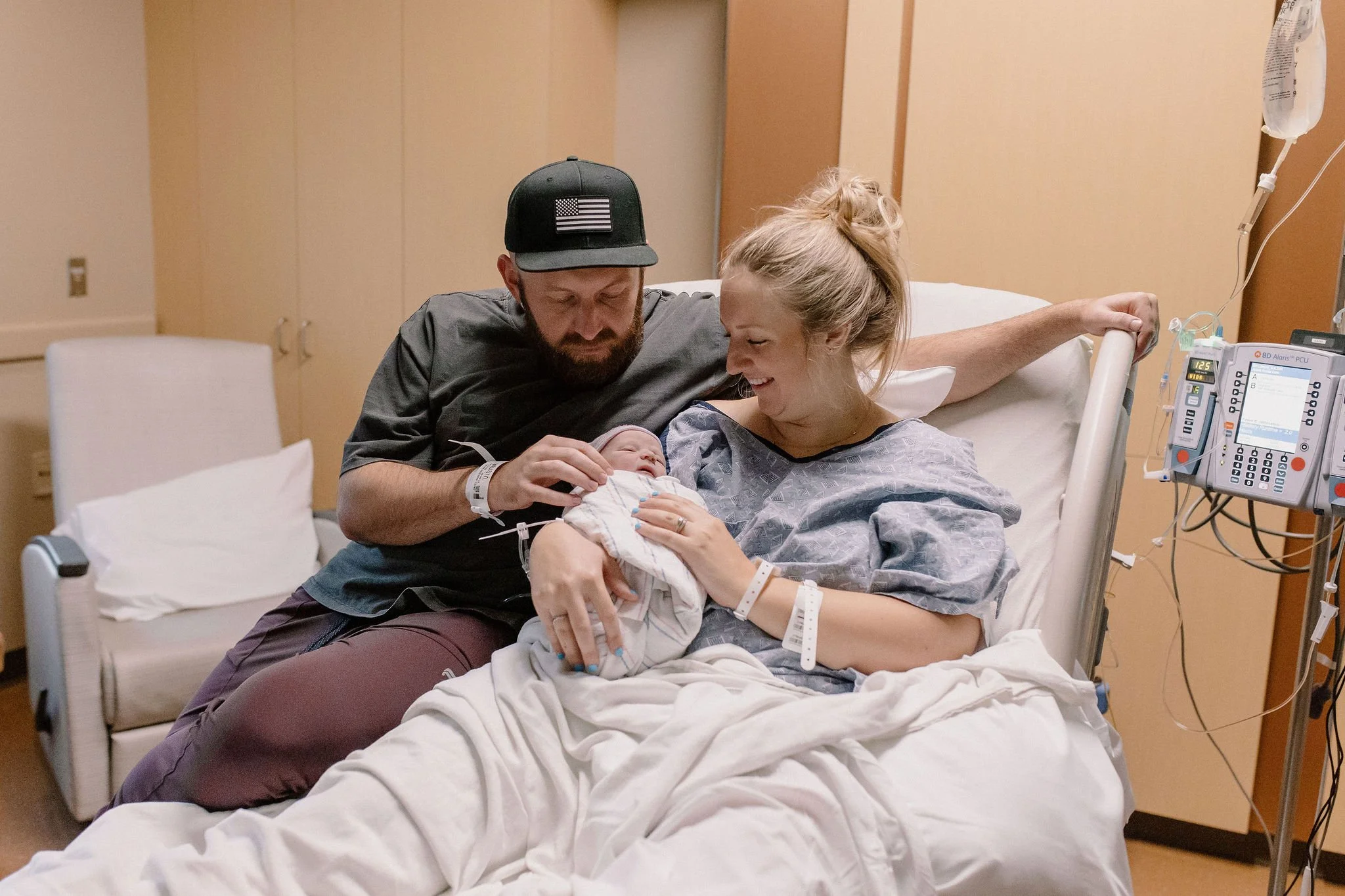 mom and dad holding swaddled newborn baby in hospital bed after birth