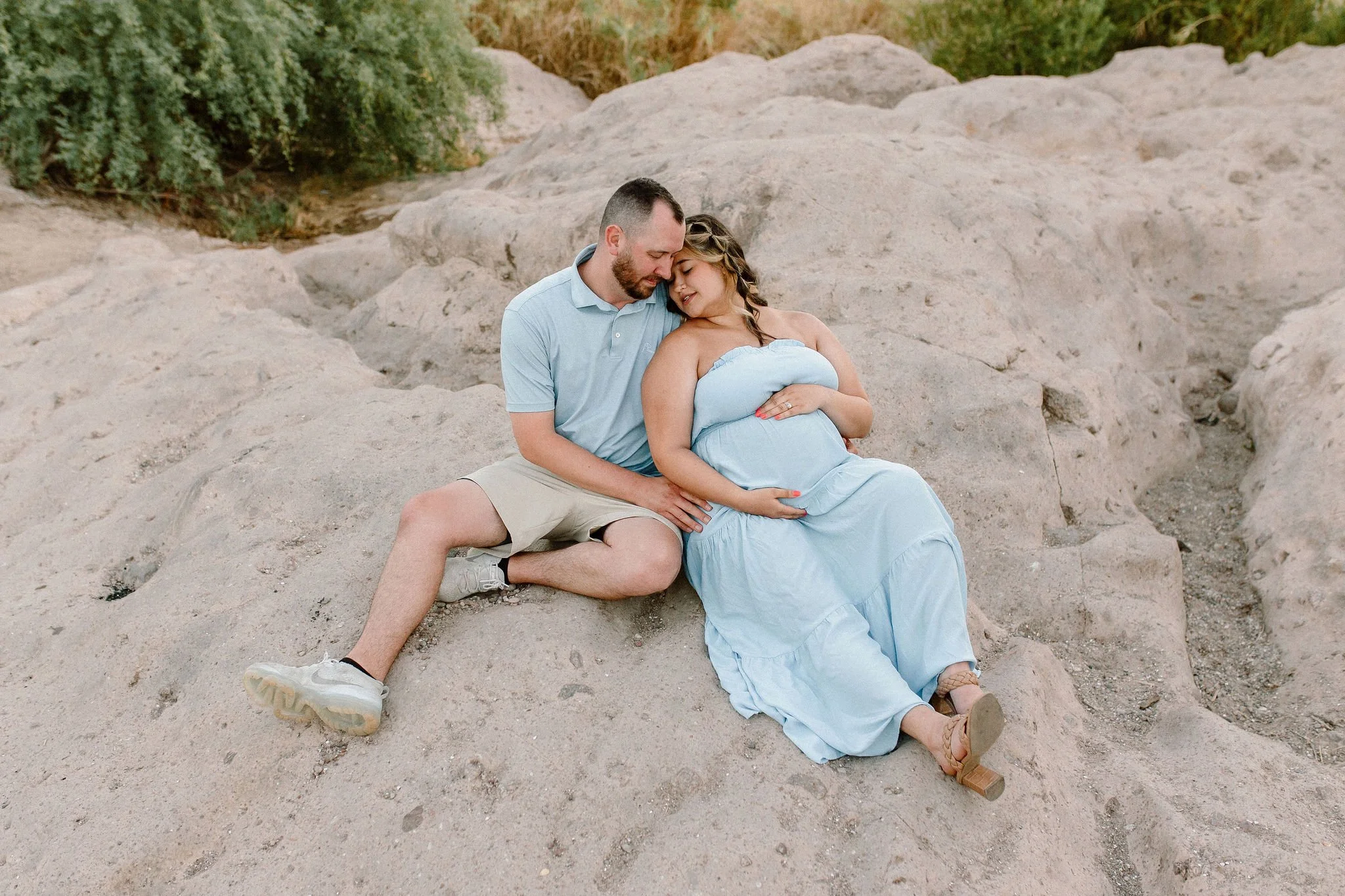 Pregnant mom sitting together holding belly on rocks near the Salt River in Scottsdale, AZ