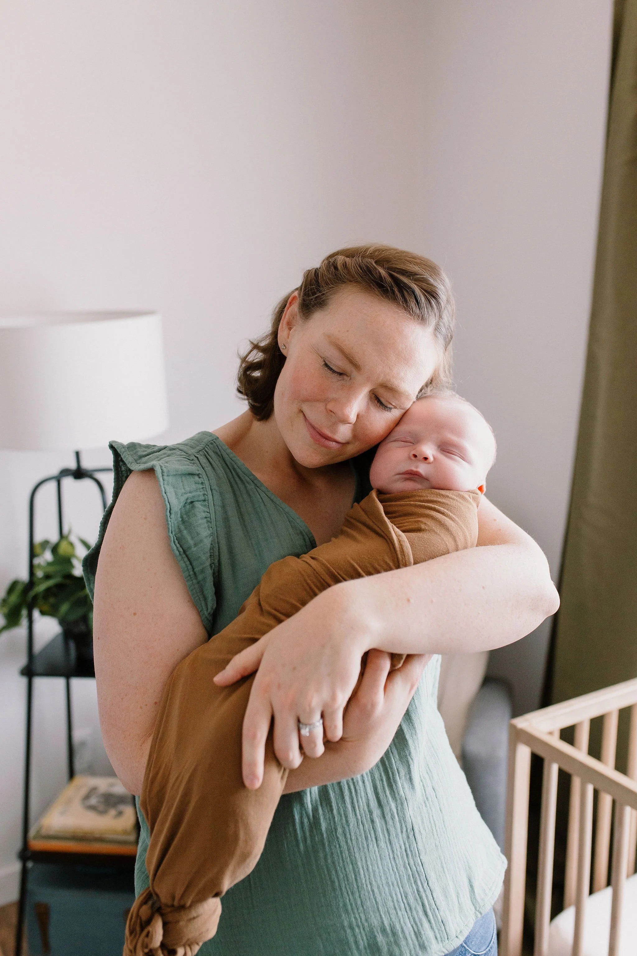 mom holding swaddled baby in nursery captured by newborn photographer